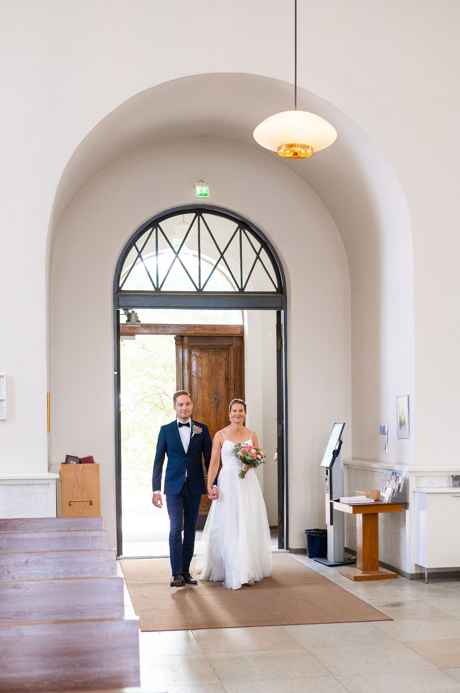 Bride and groom entering a church through an arched doorway holding hands.