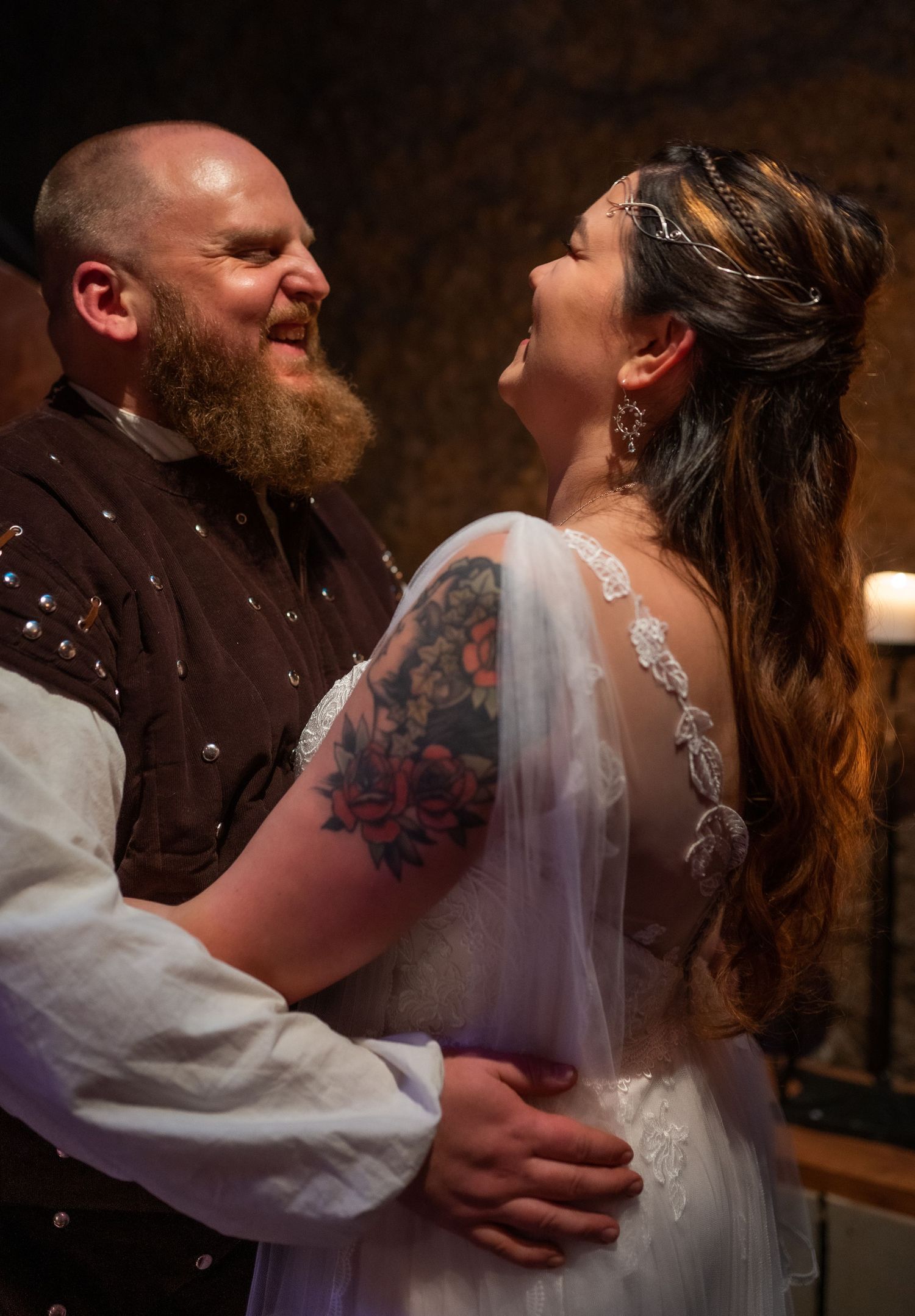 Bride and groom share a joyful moment at their medieval-themed wedding, with tattoos and a delicate crown.