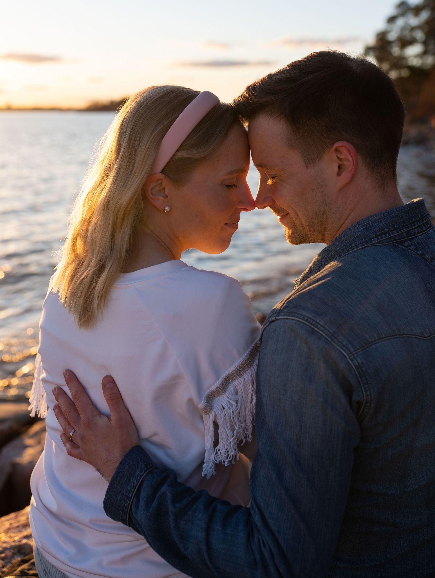 Couple touching foreheads tenderly at golden sunset by the water.