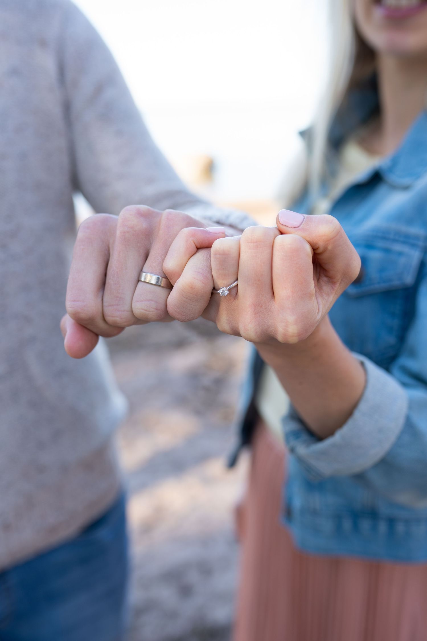 Close-up of engaged couple linking pinky fingers, both wearing silver wedding rings.
