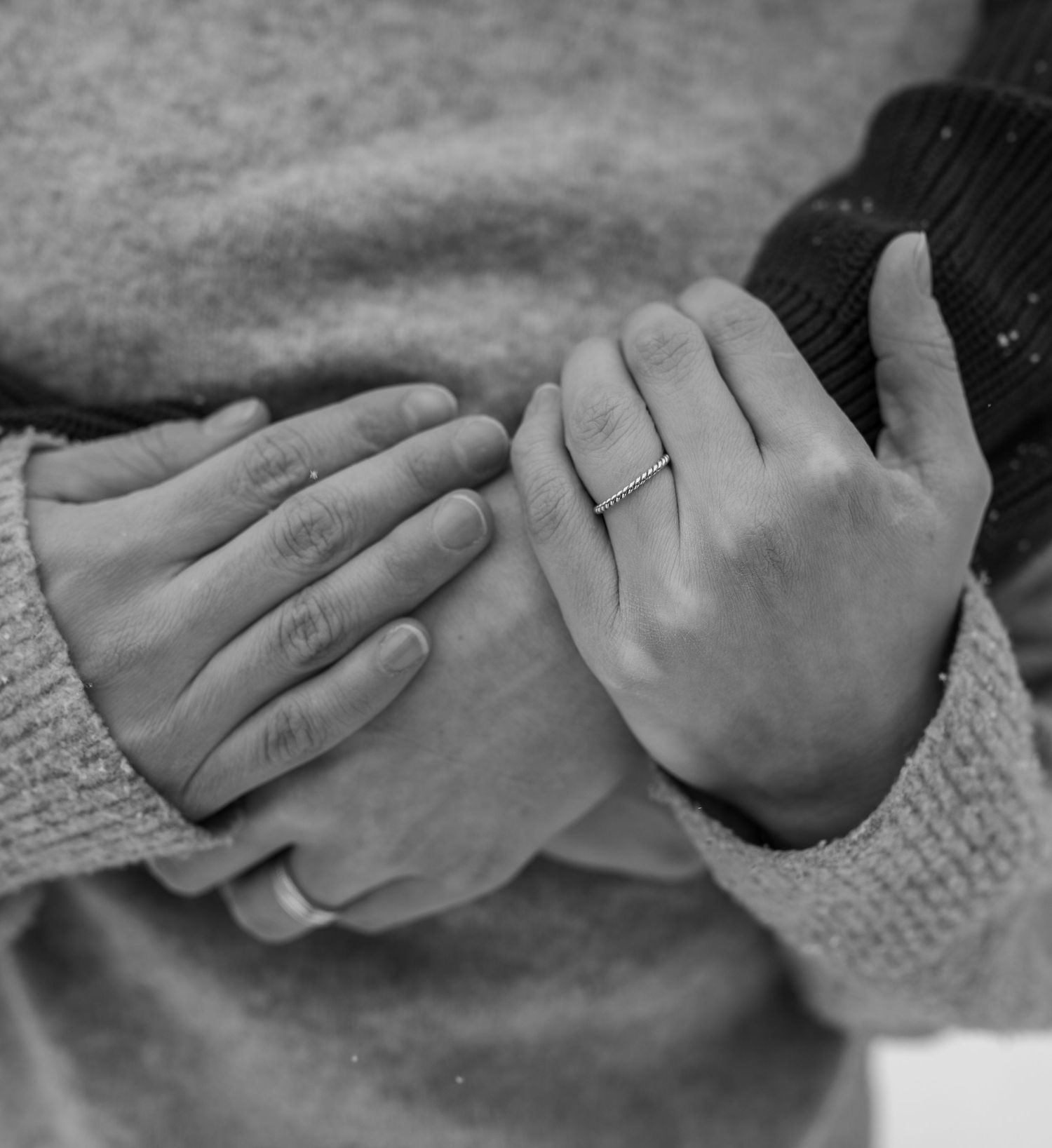 Black and white photo of two hands intertwined, one wearing a wedding ring, both in cozy sweaters.