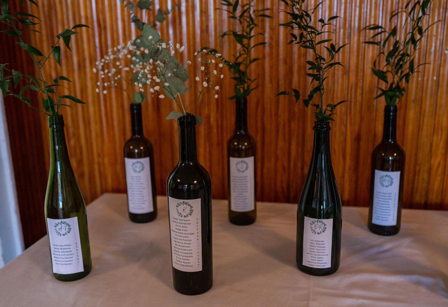 Wine bottles used as rustic vases with greenery and baby breath wedding centerpieces.