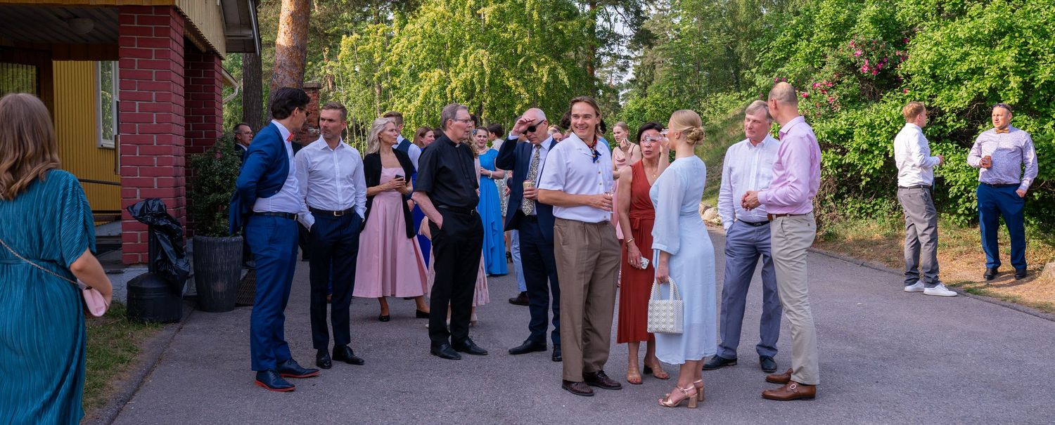Wedding guests socializing outdoors on a sunny tree-lined path after the ceremony.