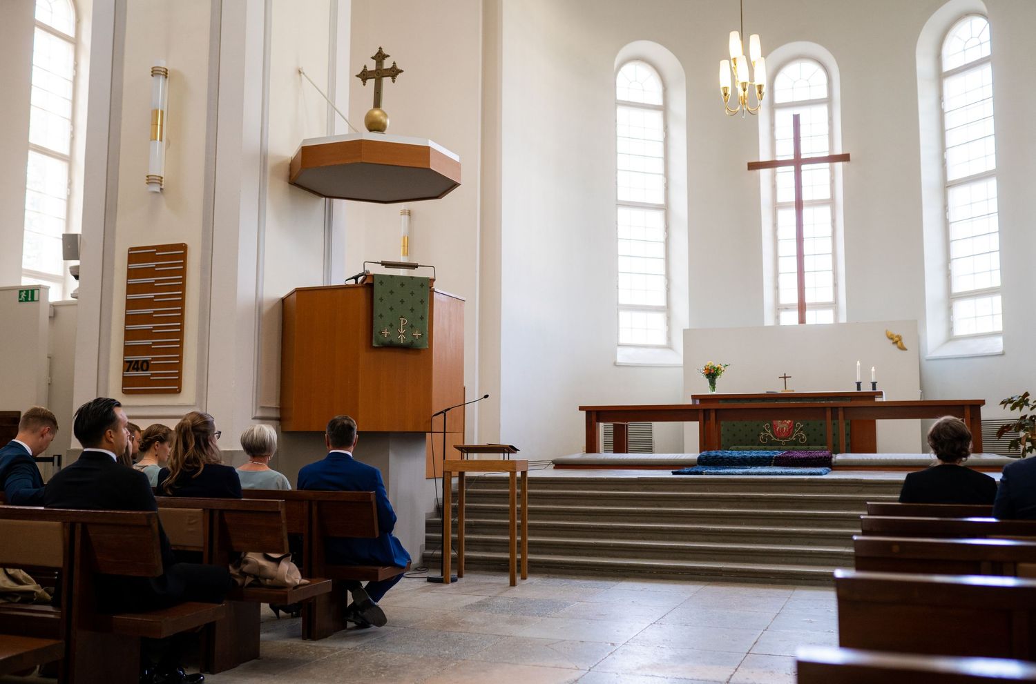 Guests seated in wooden pews during a church wedding ceremony with a pastor at the pulpit.