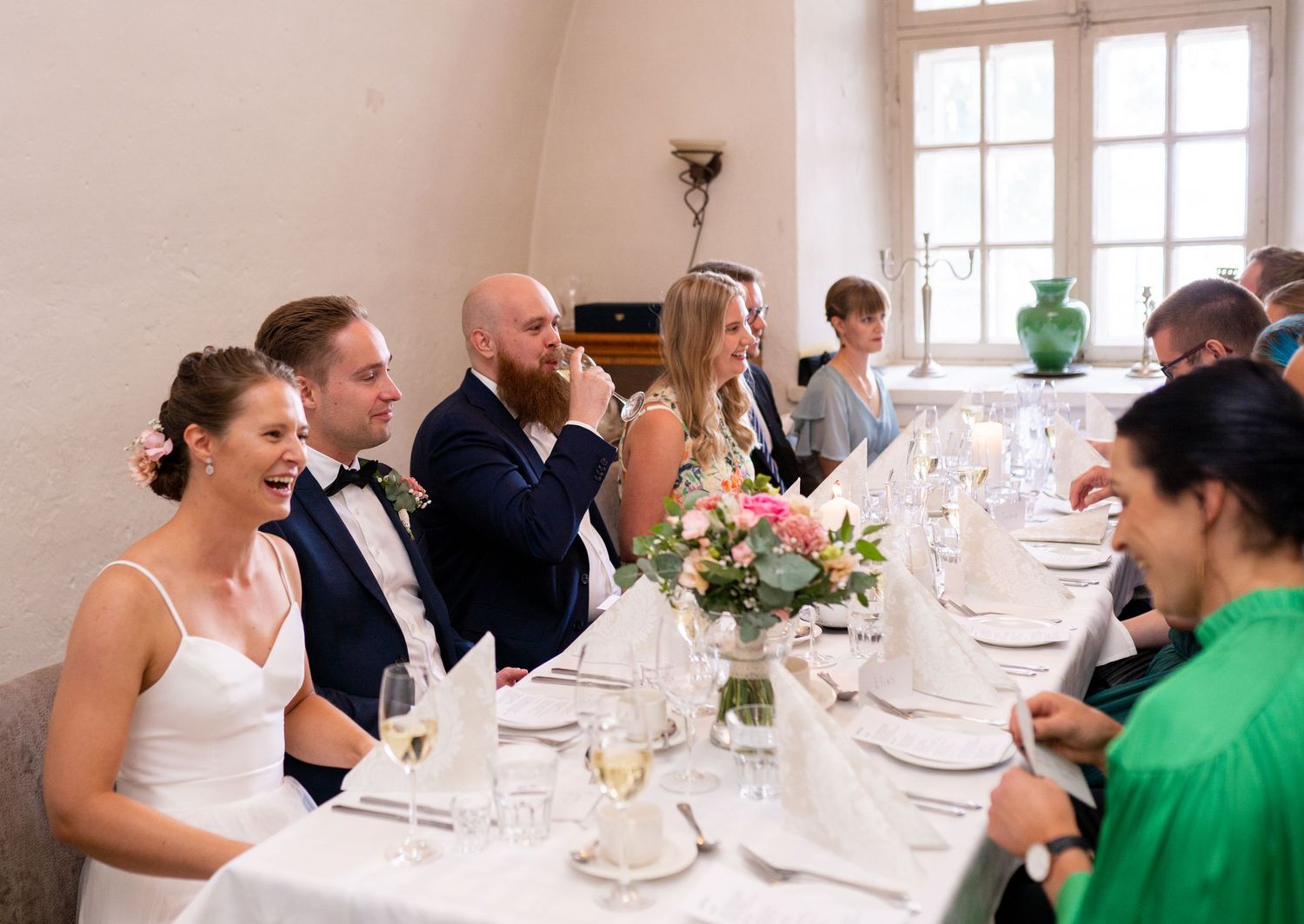 Wedding party laughing and enjoying champagne toast at elegantly set reception dinner table.