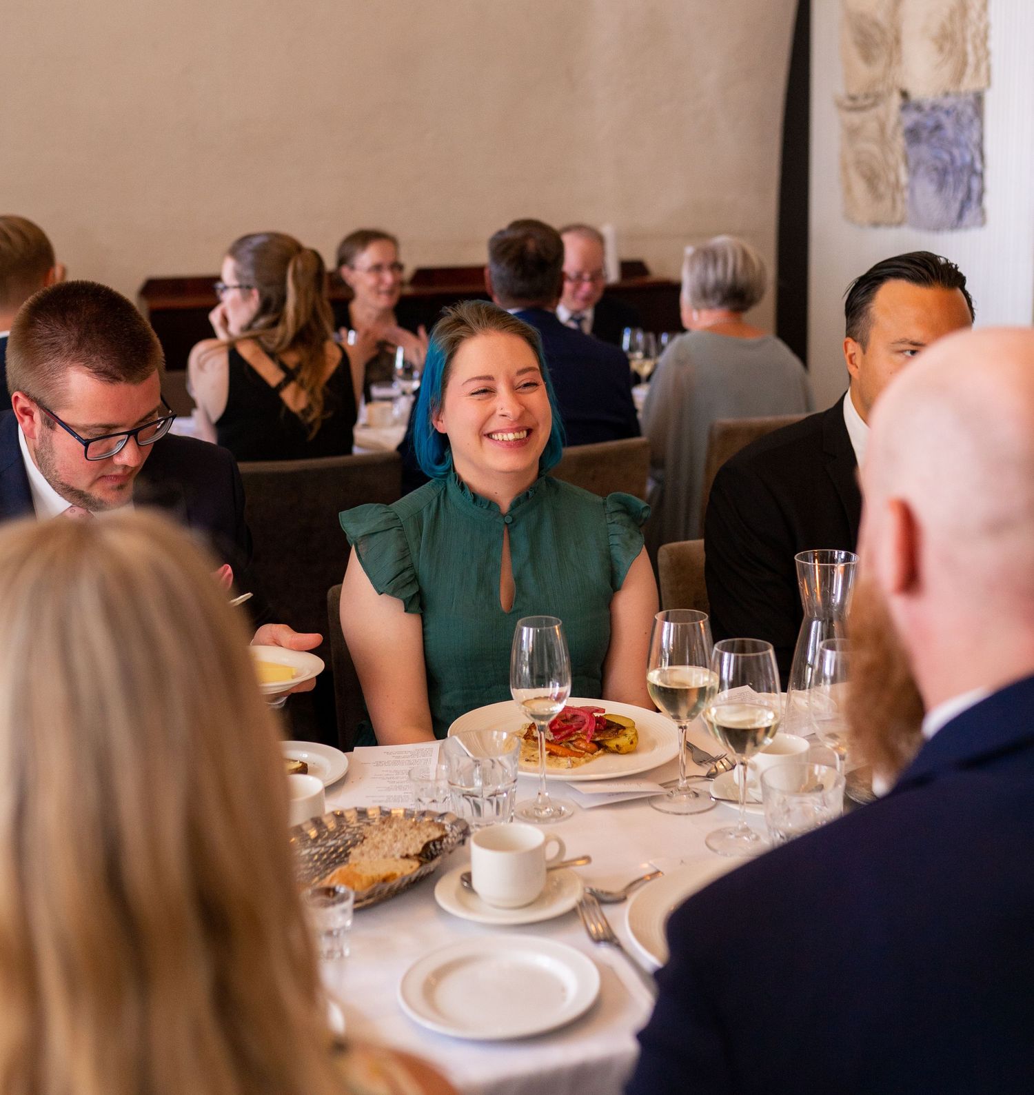 Woman in green dress laughing joyfully at a round wedding reception dinner table with guests.