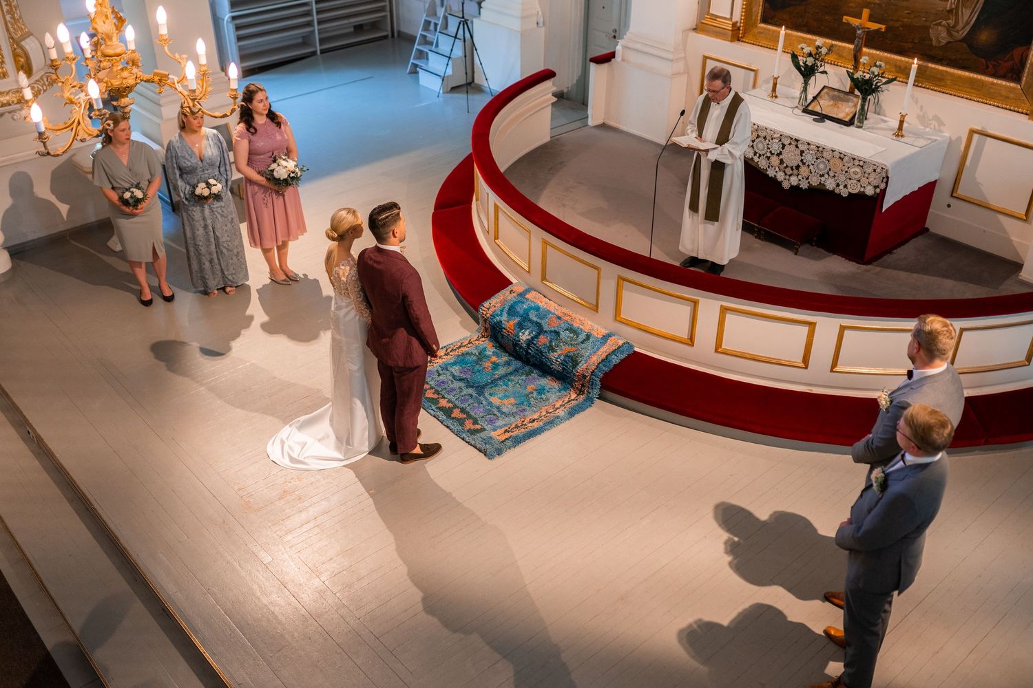 Aerial view of a wedding ceremony in a church, with bride and groom at the altar flanked by bridesmaids and officiant.