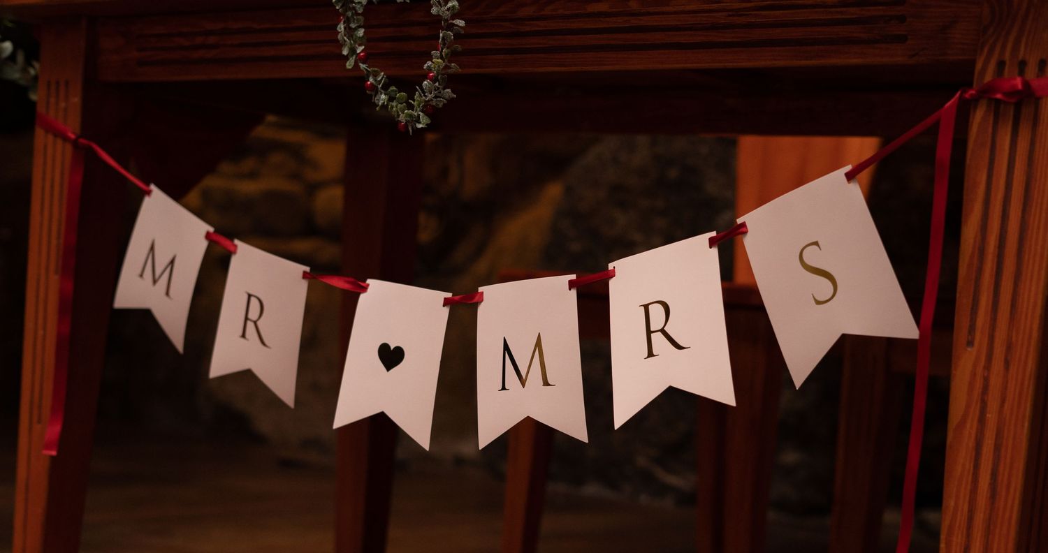 Mr and Mrs wedding banner bunting hanging on wooden posts with red ribbon accents and greenery wreath.