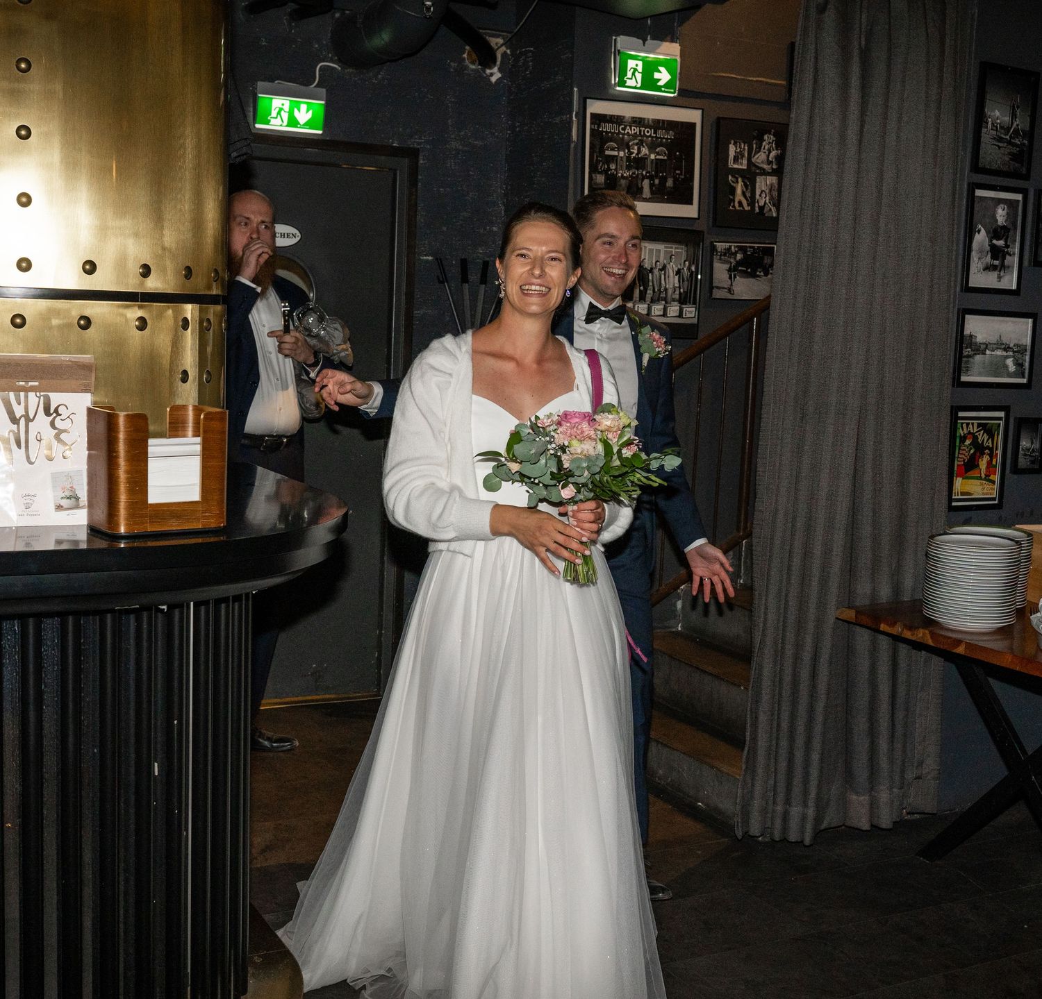 Smiling bride and groom make grand entrance at wedding reception venue with industrial decor.