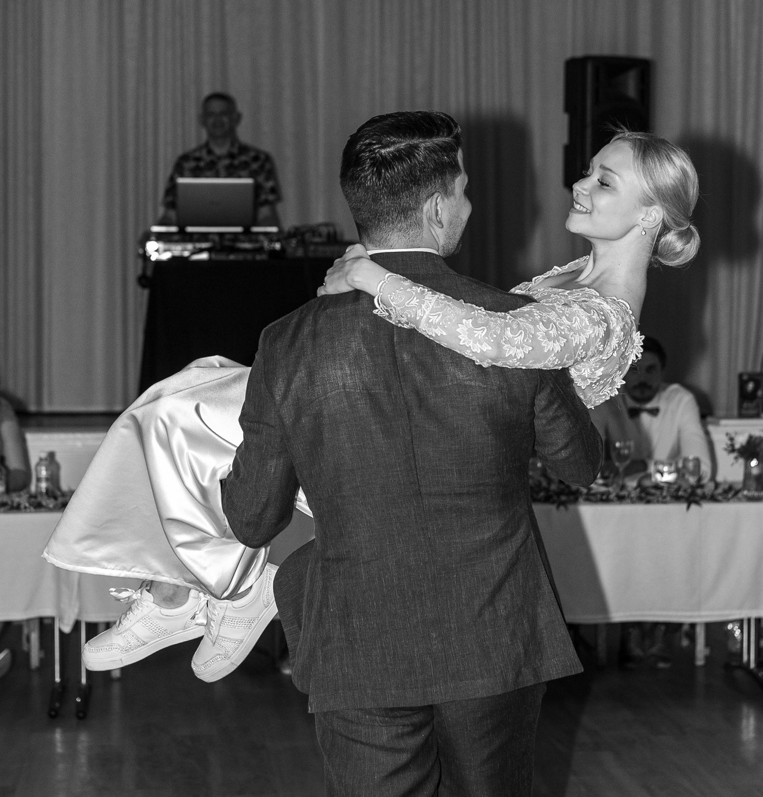 Black and white photo of bride and groom dancing at wedding reception with DJ in background.