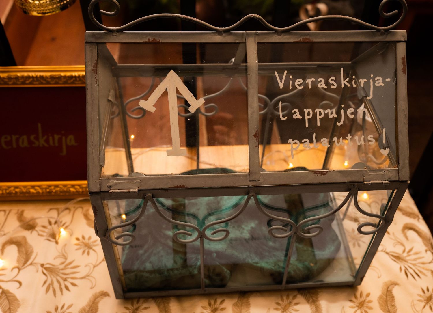Decorative glass display box with Finnish text Vieraskirja at a wedding or event venue.