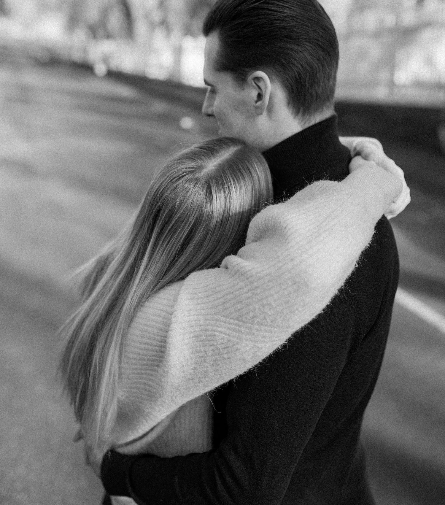 Black and white photo of a couple embracing outdoors, woman with long blonde hair hugging a man in a dark turtleneck.