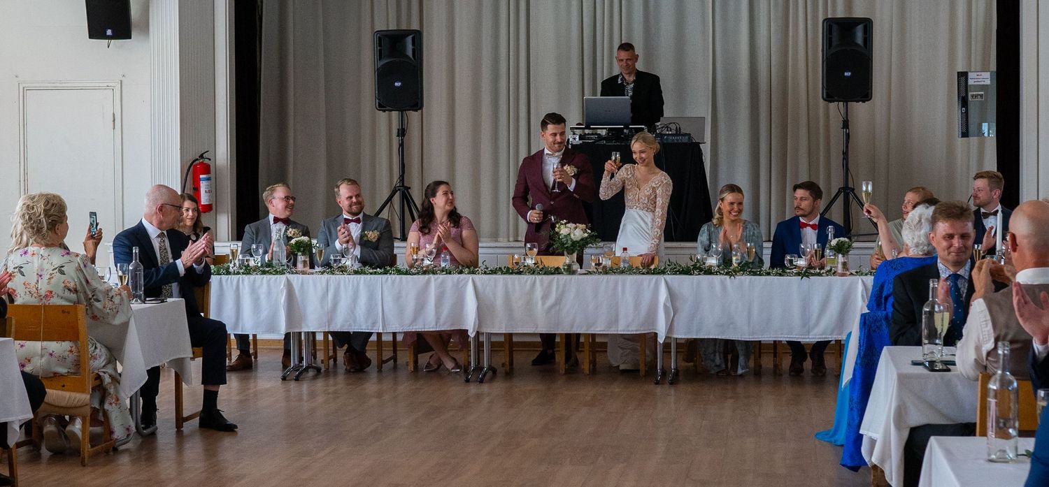 Wedding party seated at decorated head table during reception dinner celebration.