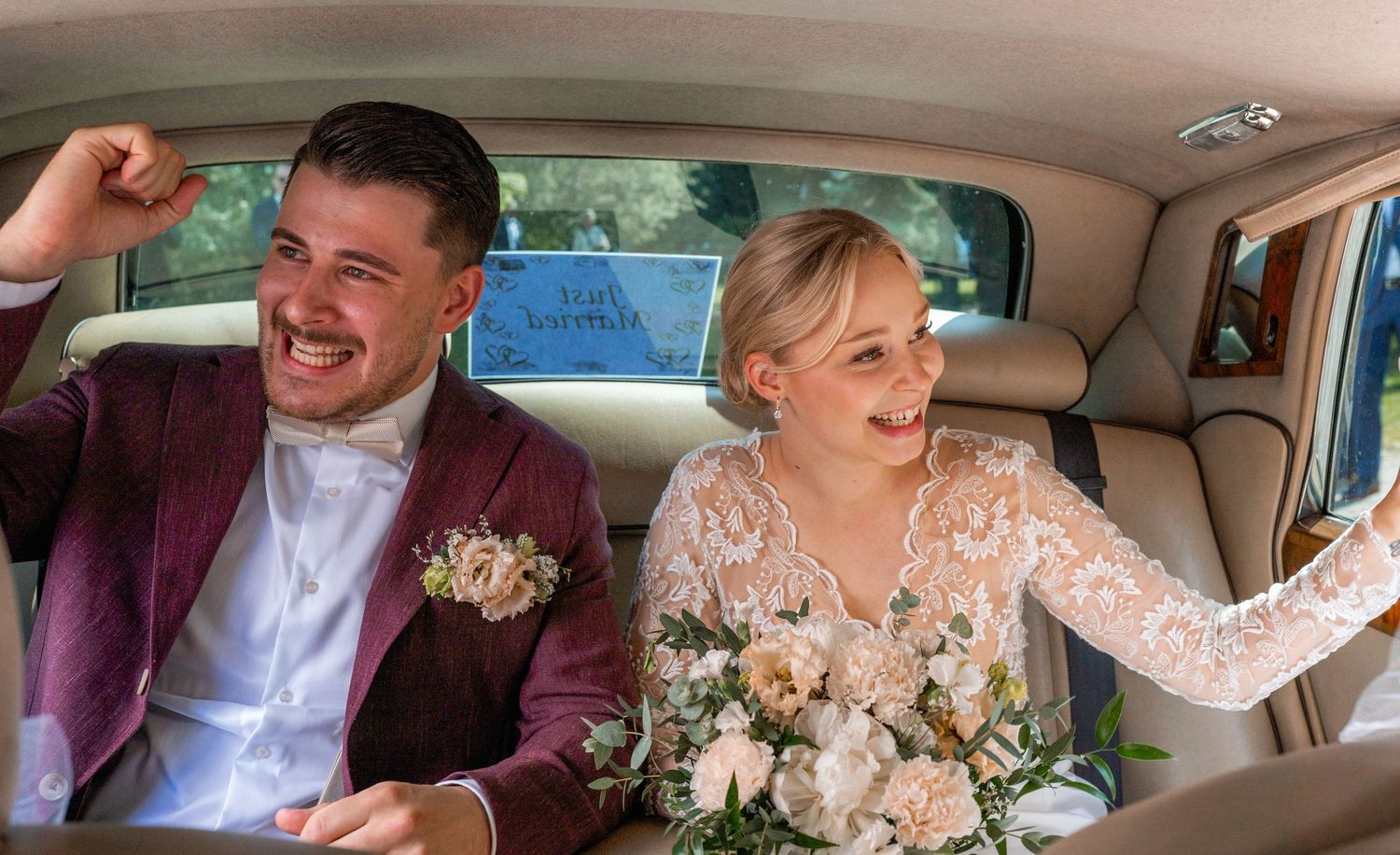 Joyful newlyweds laughing together inside a classic car on their wedding day.