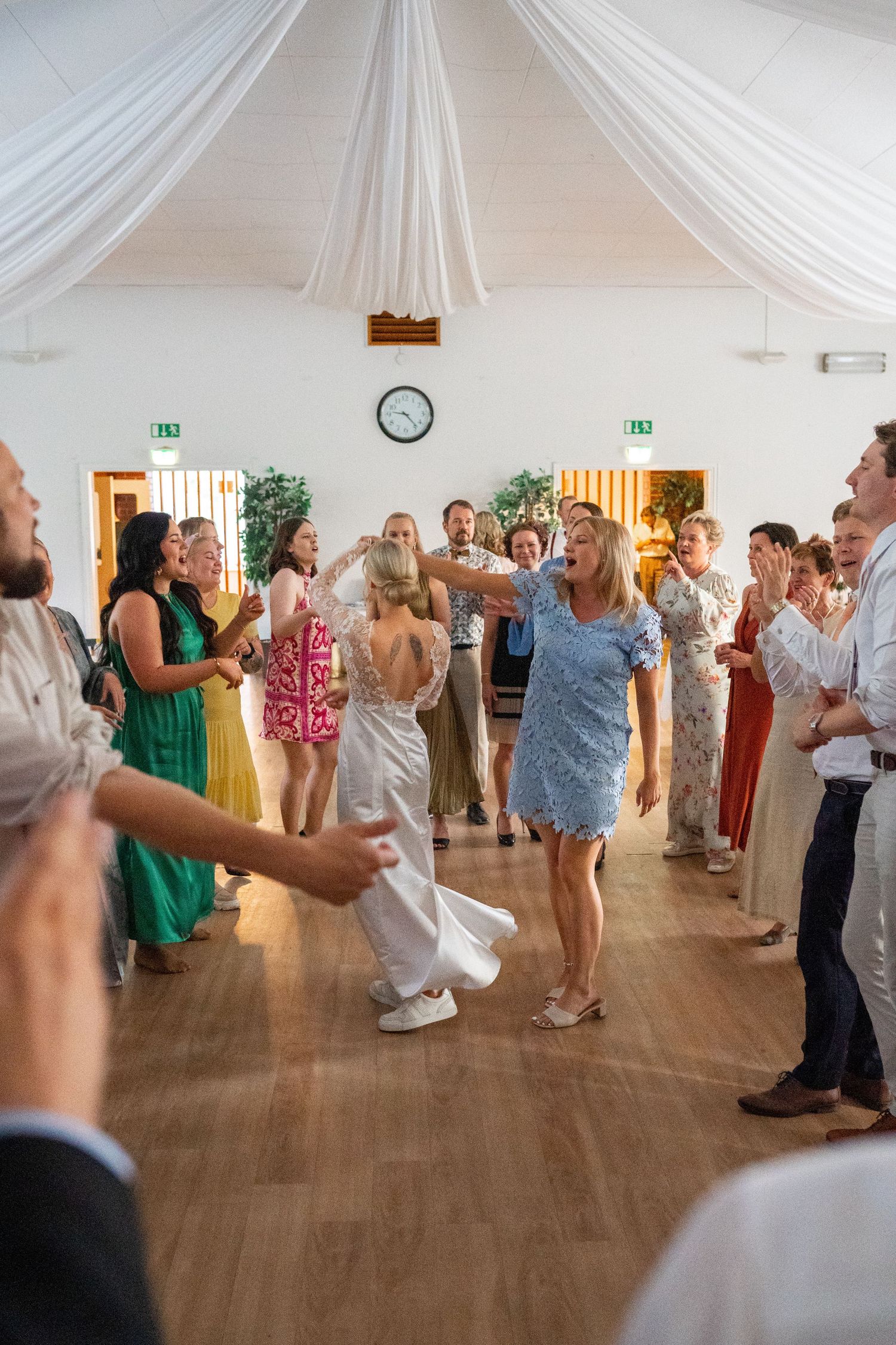 Bride and wedding guests dance joyfully in a circle on the decorated reception hall dance floor.