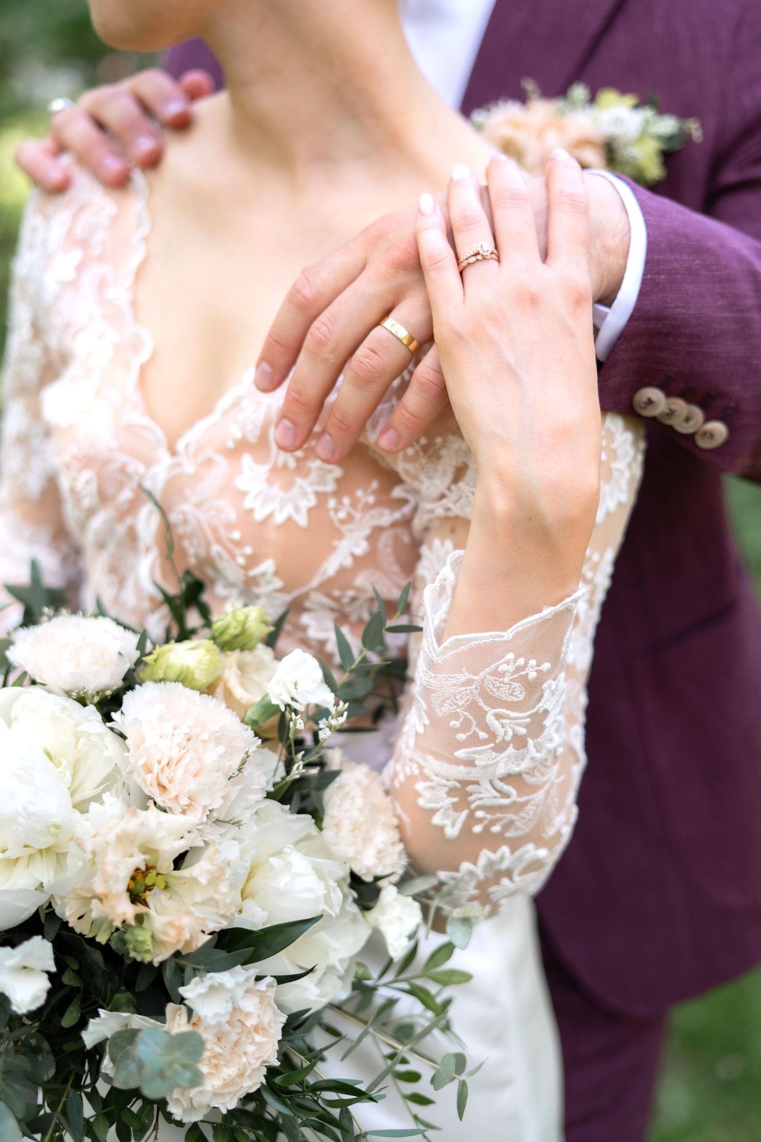 Bride and groom showing gold wedding rings, bride holding white peony bouquet in lace wedding dress.