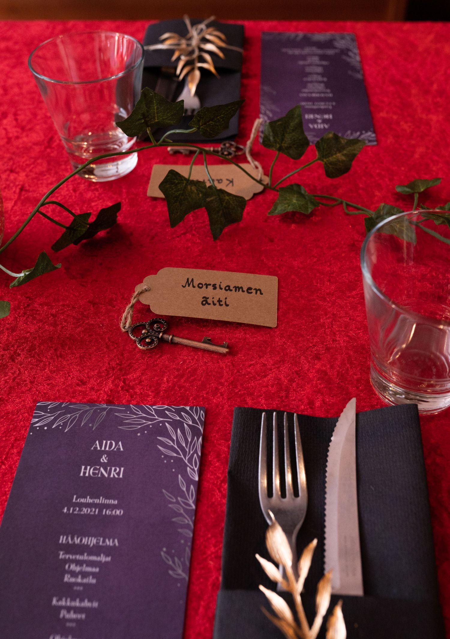 Elegant wedding table setting with red tablecloth, navy blue menu cards, ivy, and a place card reading Morsiamen Siiti.