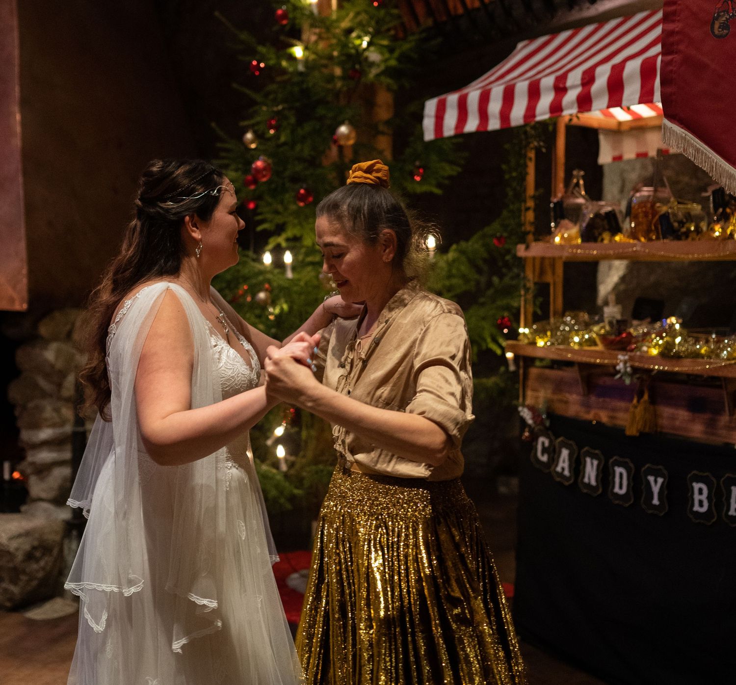 Two women share a joyful moment near a Christmas tree and candy bar at a festive holiday wedding celebration.