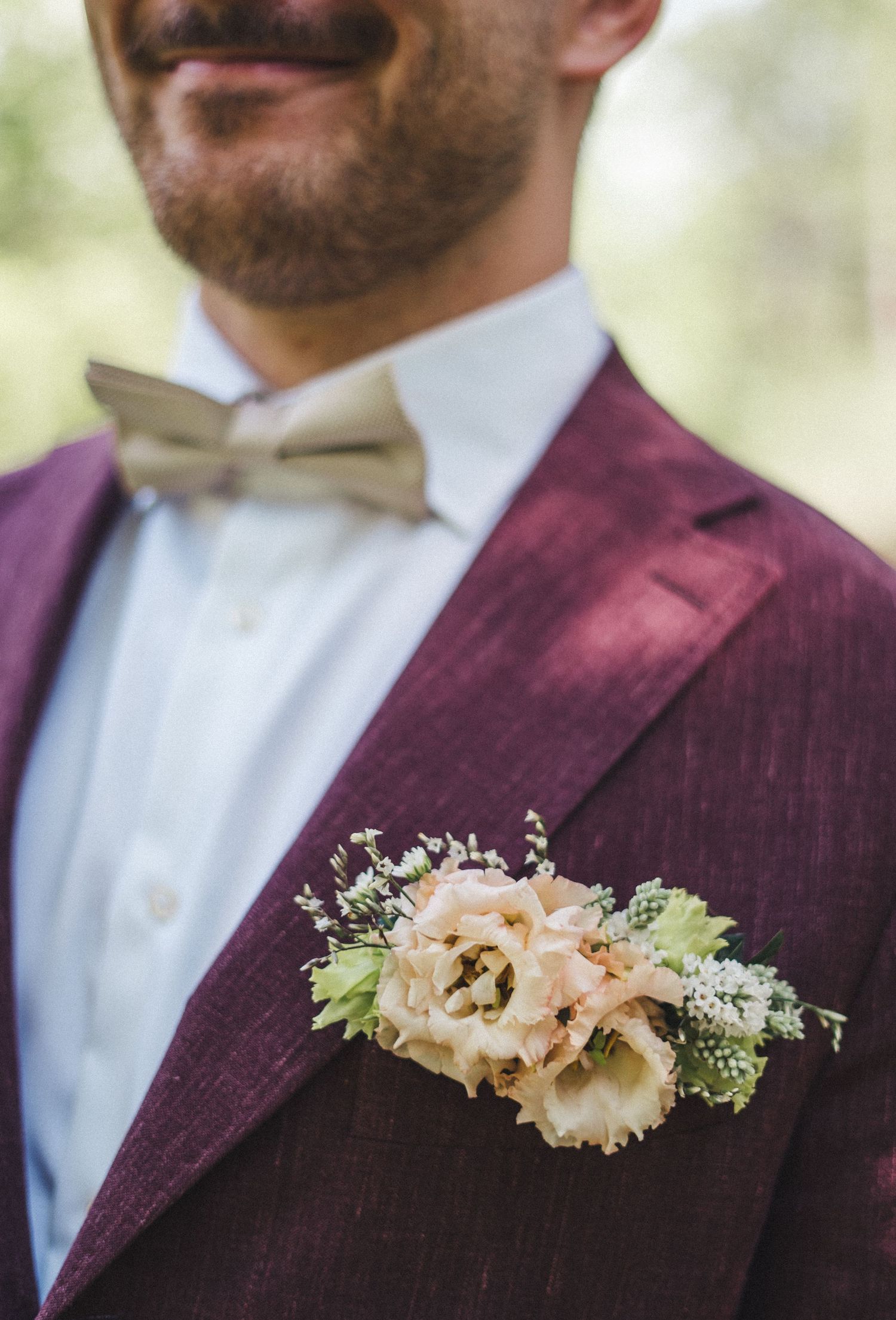 Close-up of groom's burgundy suit lapel with cream floral boutonniere and bow tie.