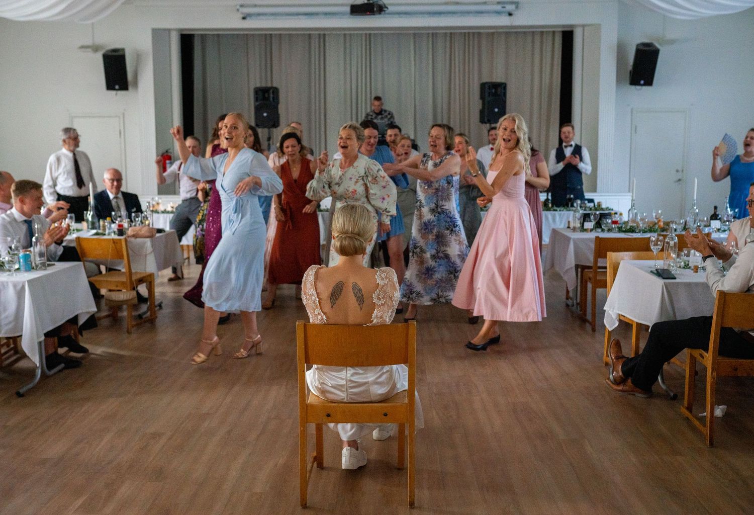 Wedding guests perform a choreographed dance surprise for the bride seated in a chair at the reception.