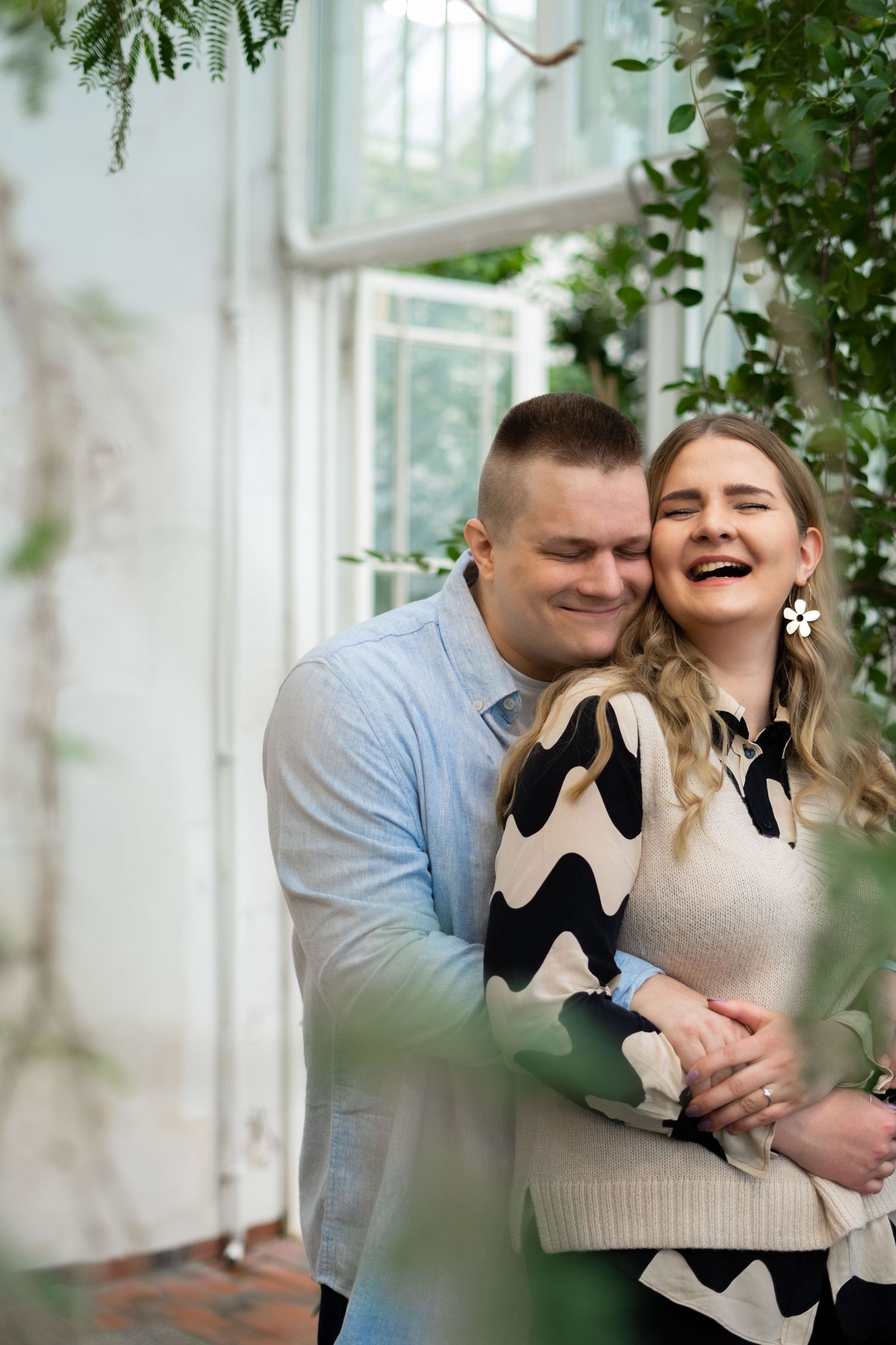 Happy couple hugging and laughing in a lush greenhouse setting.