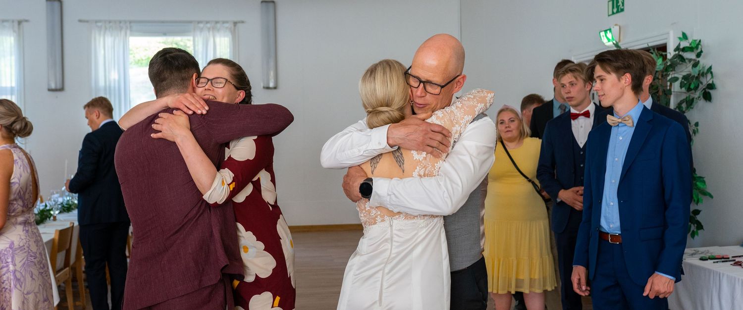 Bride and groom embrace family members during wedding reception guest greeting line.