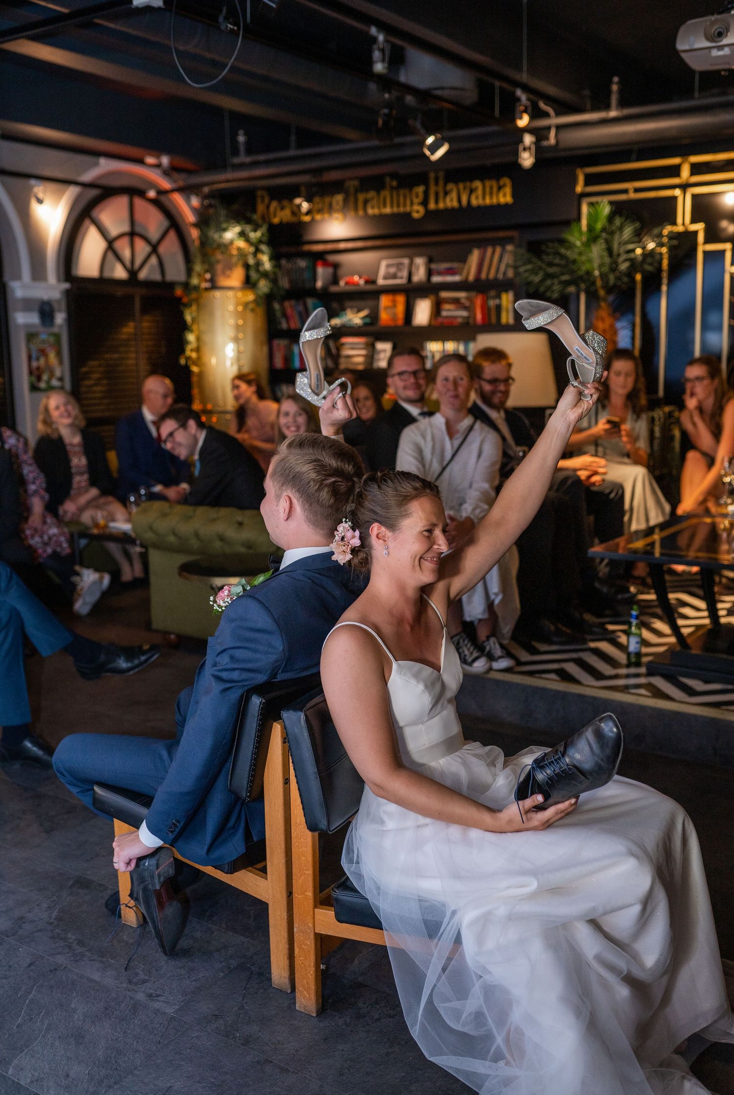 Bride and groom playing shoe game at wedding reception while guests watch and laugh.