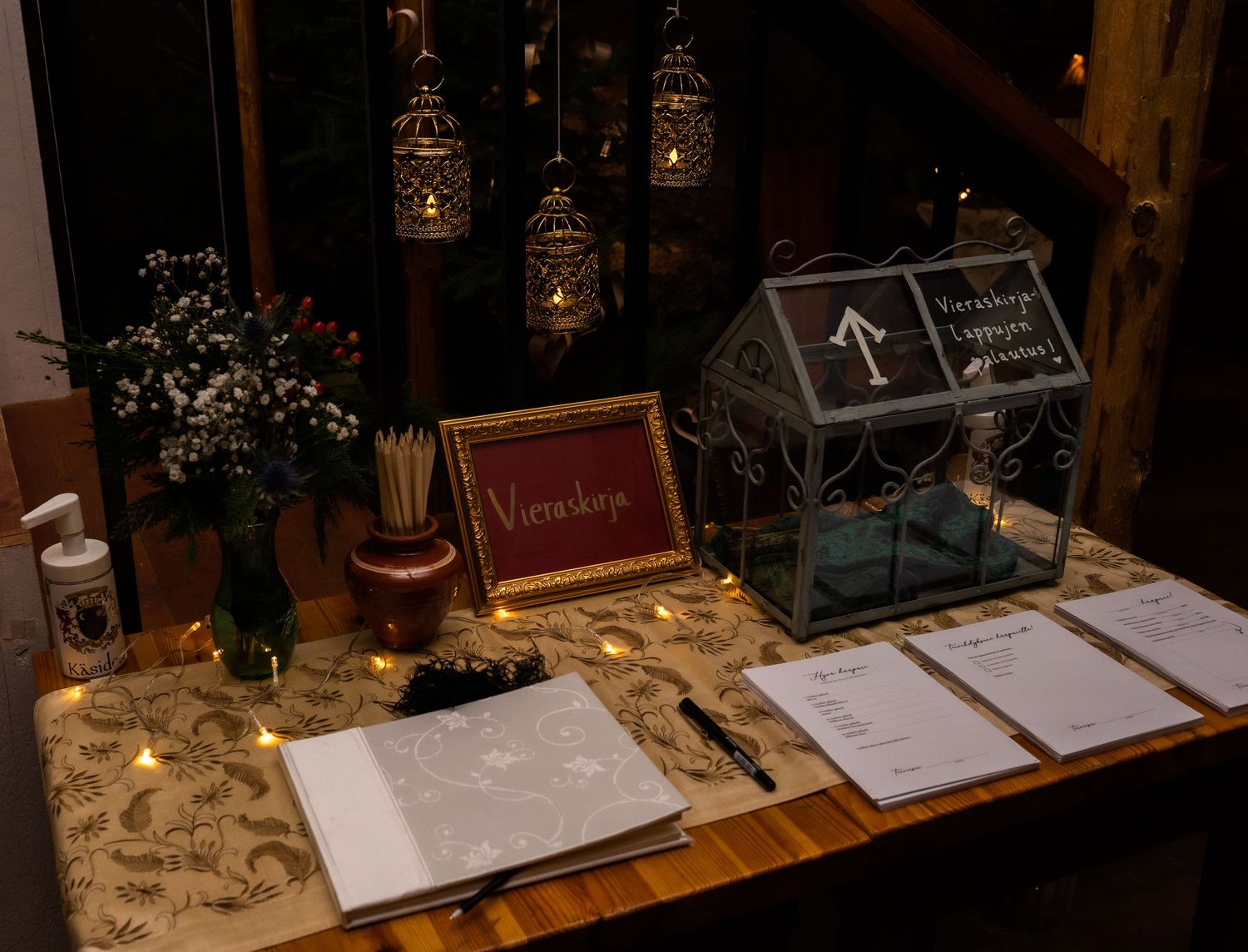 Elegant wedding reception table with guest book, card box, fairy lights, and floral arrangements in warm ambiance.