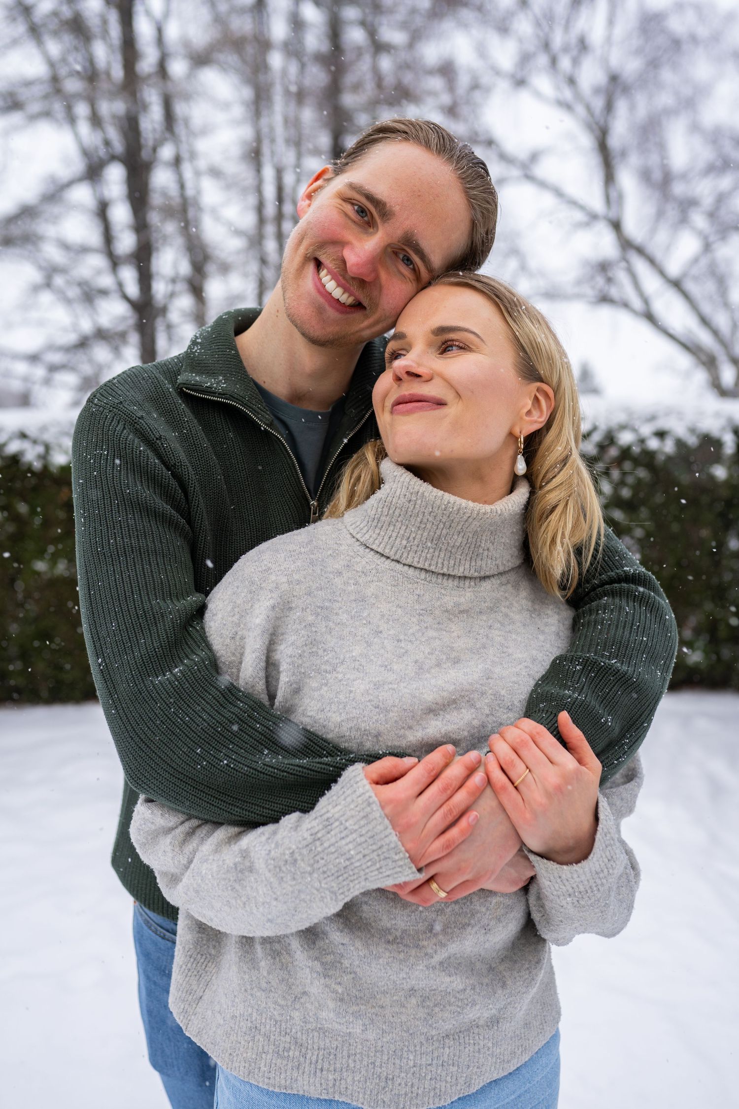 A happy couple embraces in a snowy winter setting, wearing cozy sweaters, smiling warmly together outdoors.