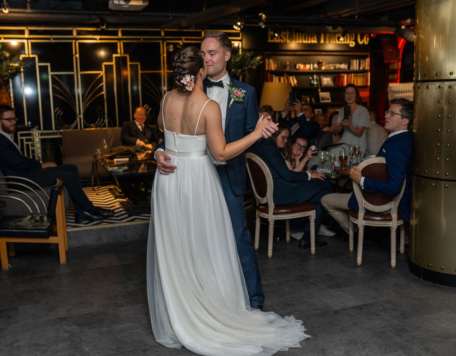 Bride and groom share intimate first dance at elegant wedding reception with guests seated at tables behind them.