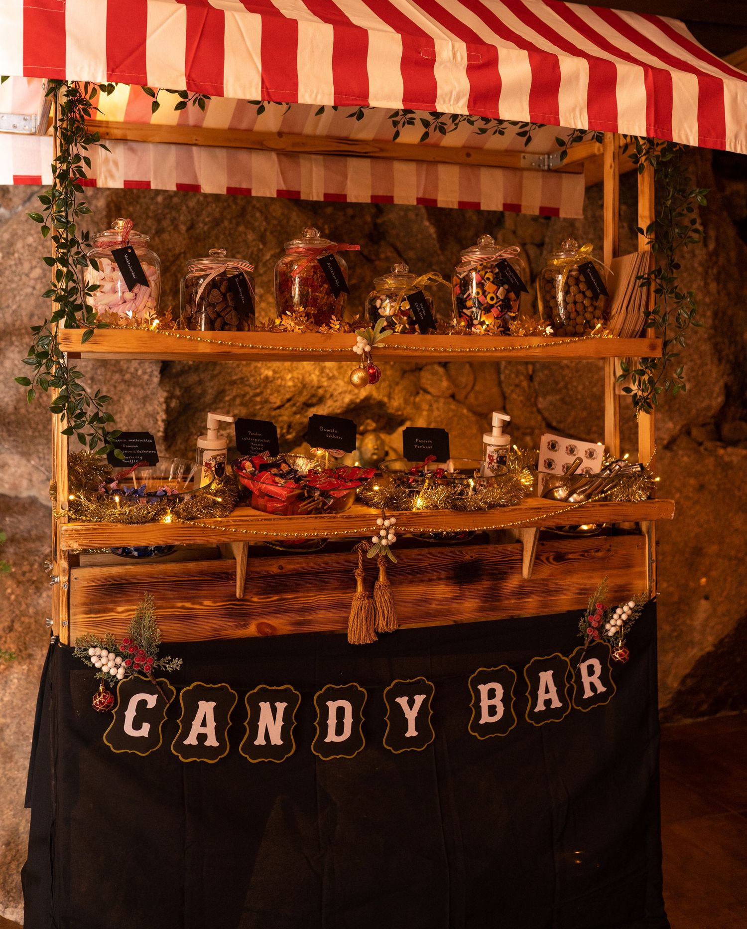 Rustic wooden candy bar display with glass jars of sweets, red striped awning, and decorative bunting sign.