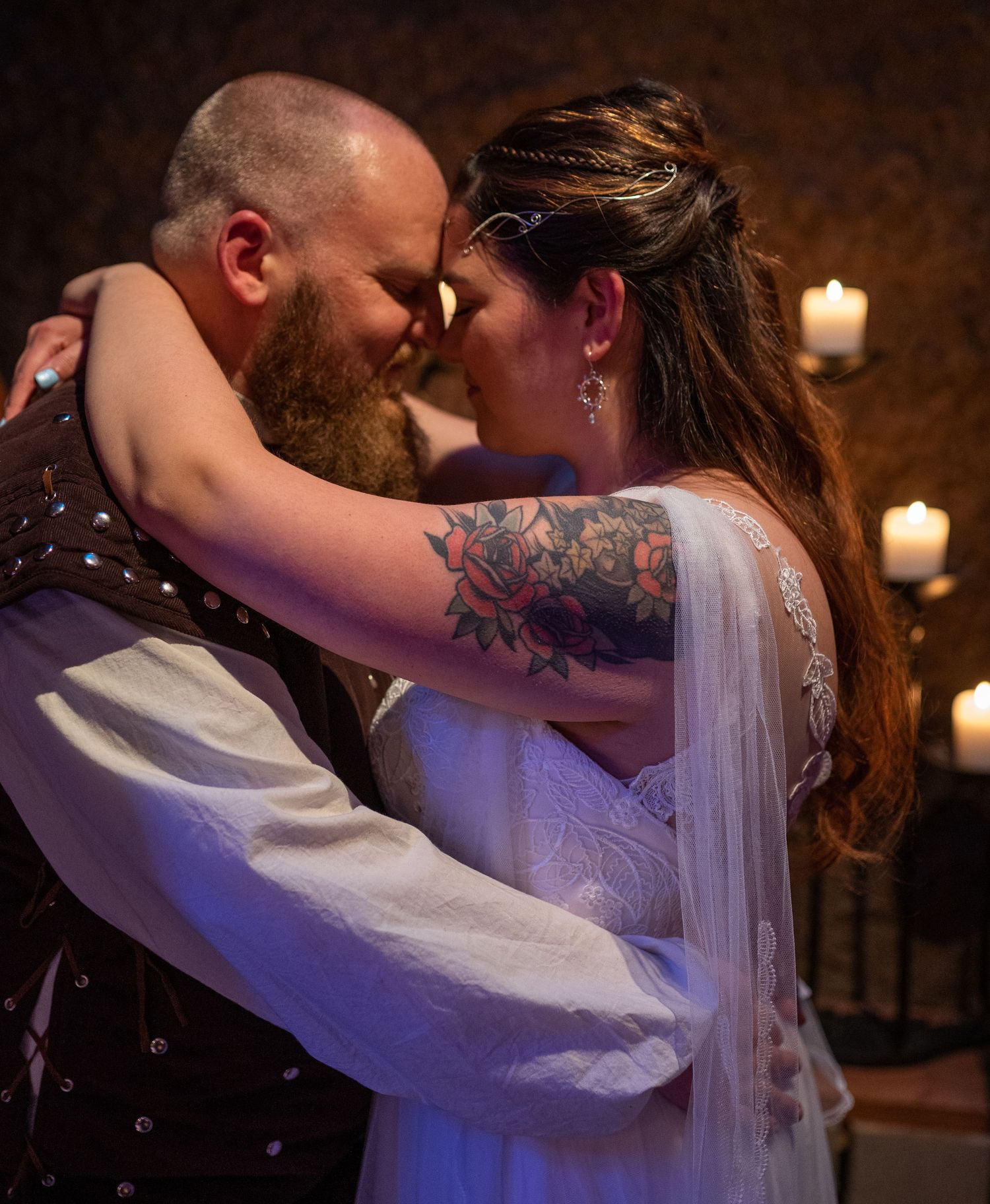 A bride and groom share an intimate forehead touch during their wedding ceremony, with candlelight glowing in the background.