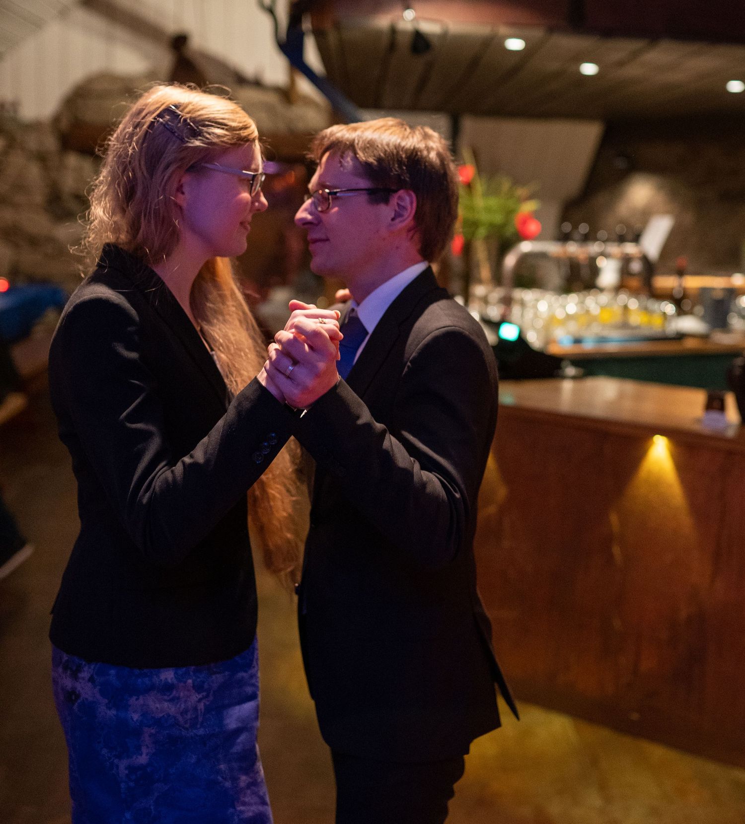 Couple dancing together in a dimly lit bar, dressed in formal attire, sharing a romantic moment.