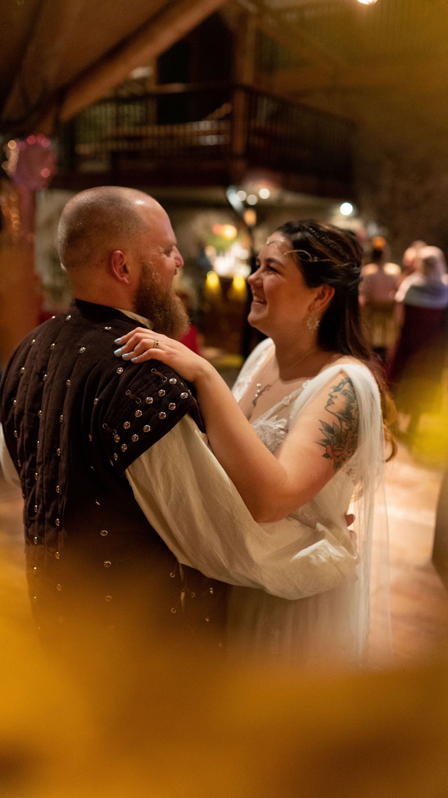 Bride and groom share first dance at rustic wedding venue, bride wearing white gown with veil and floral crown.