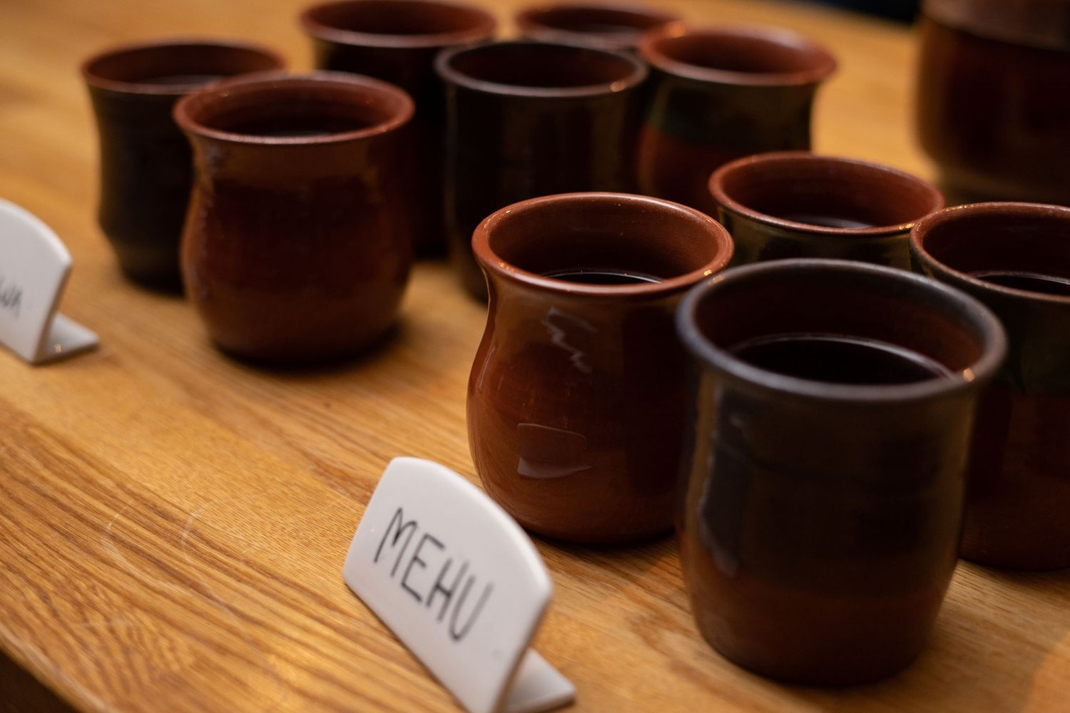 Rustic brown clay cups arranged on a wooden table with a handwritten menu sign at a traditional restaurant.