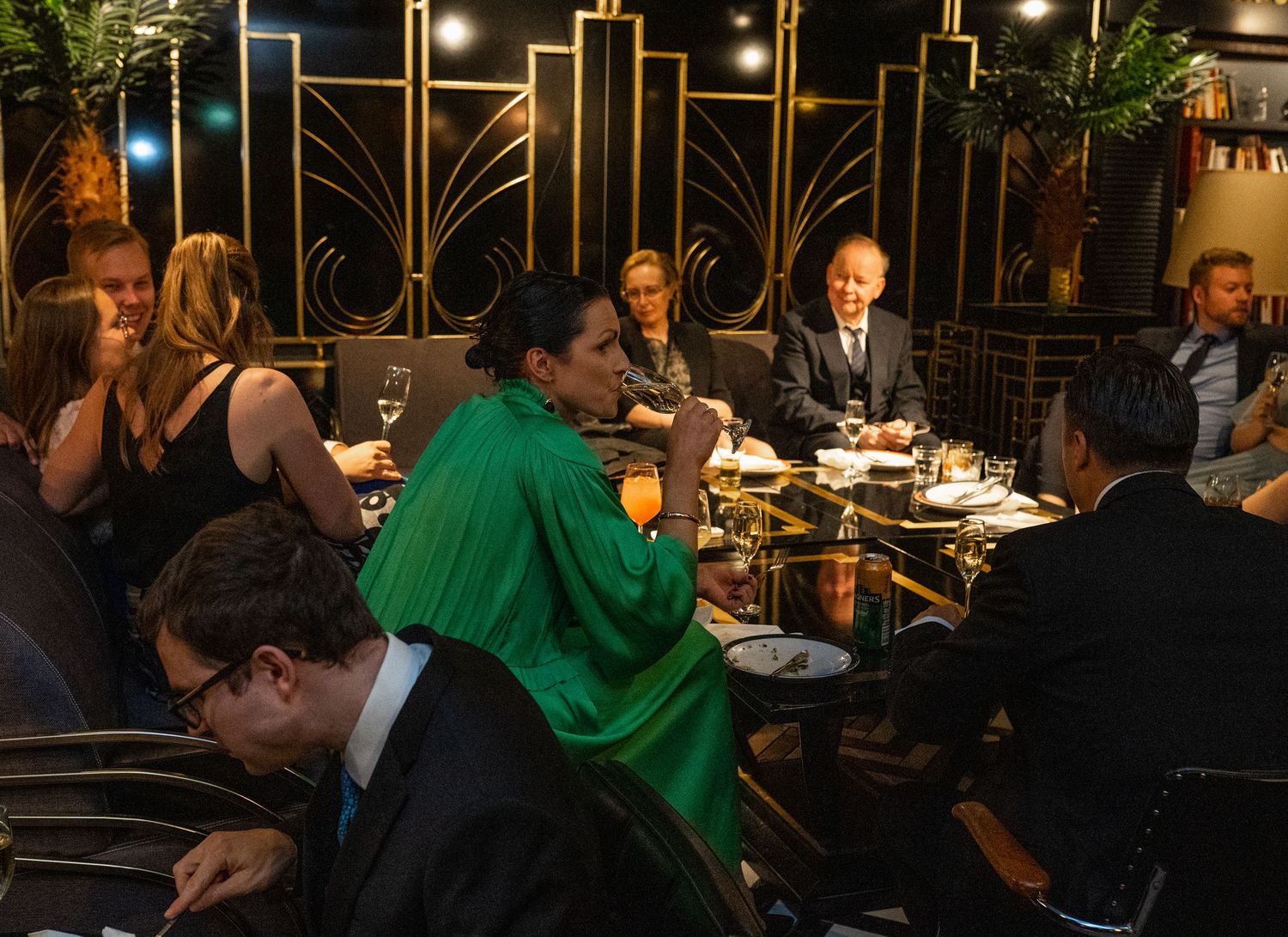 Guests in formal attire dining at elegant gold Art Deco restaurant during wedding reception.