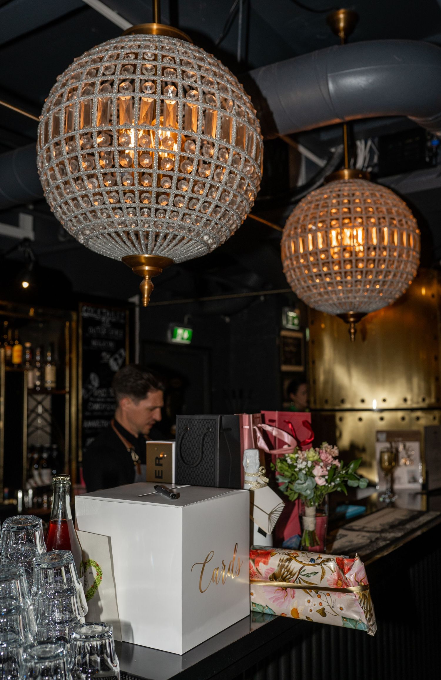 Elegant crystal globe pendant lights above bar with gift boxes and flowers at event.