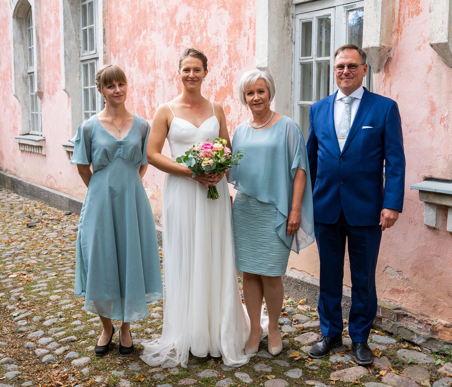 Bride in white gown holds pink bouquet posing with three family members in teal dresses and blue suit.