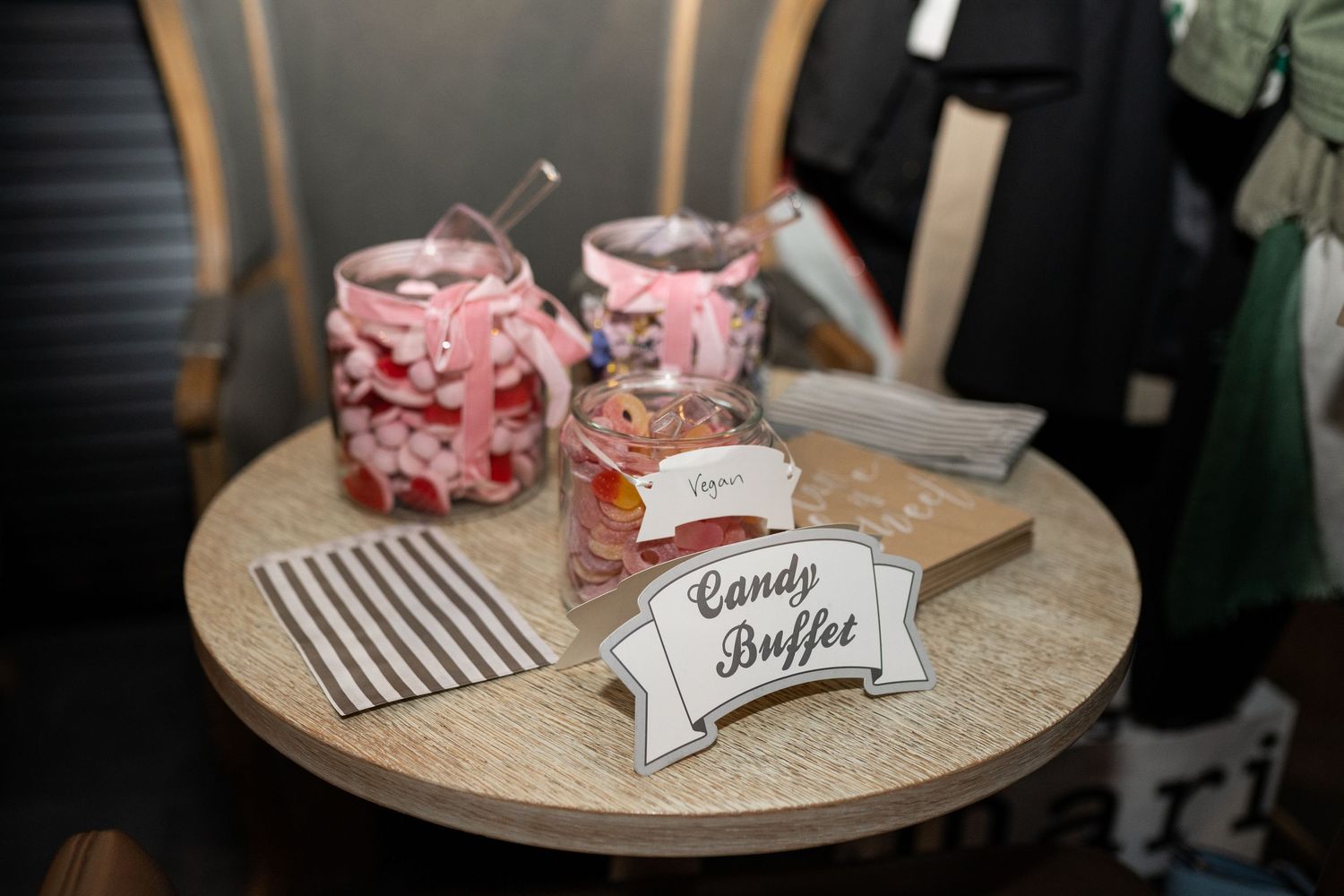 Candy buffet display with pink sweets in glass jars on round wooden table at wedding reception.