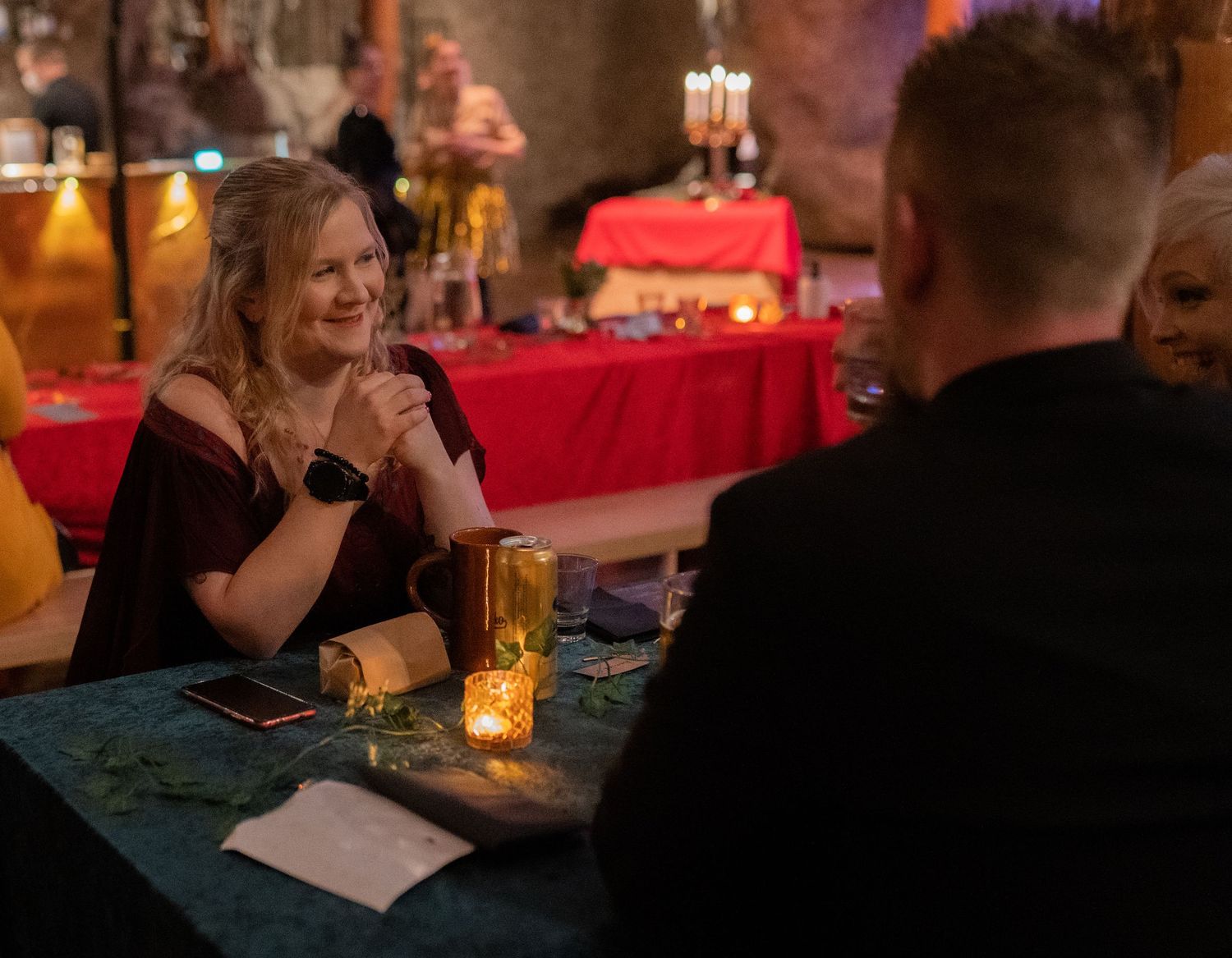 Woman smiling at candlelit dinner table in elegant venue with red tablecloth decor in background.