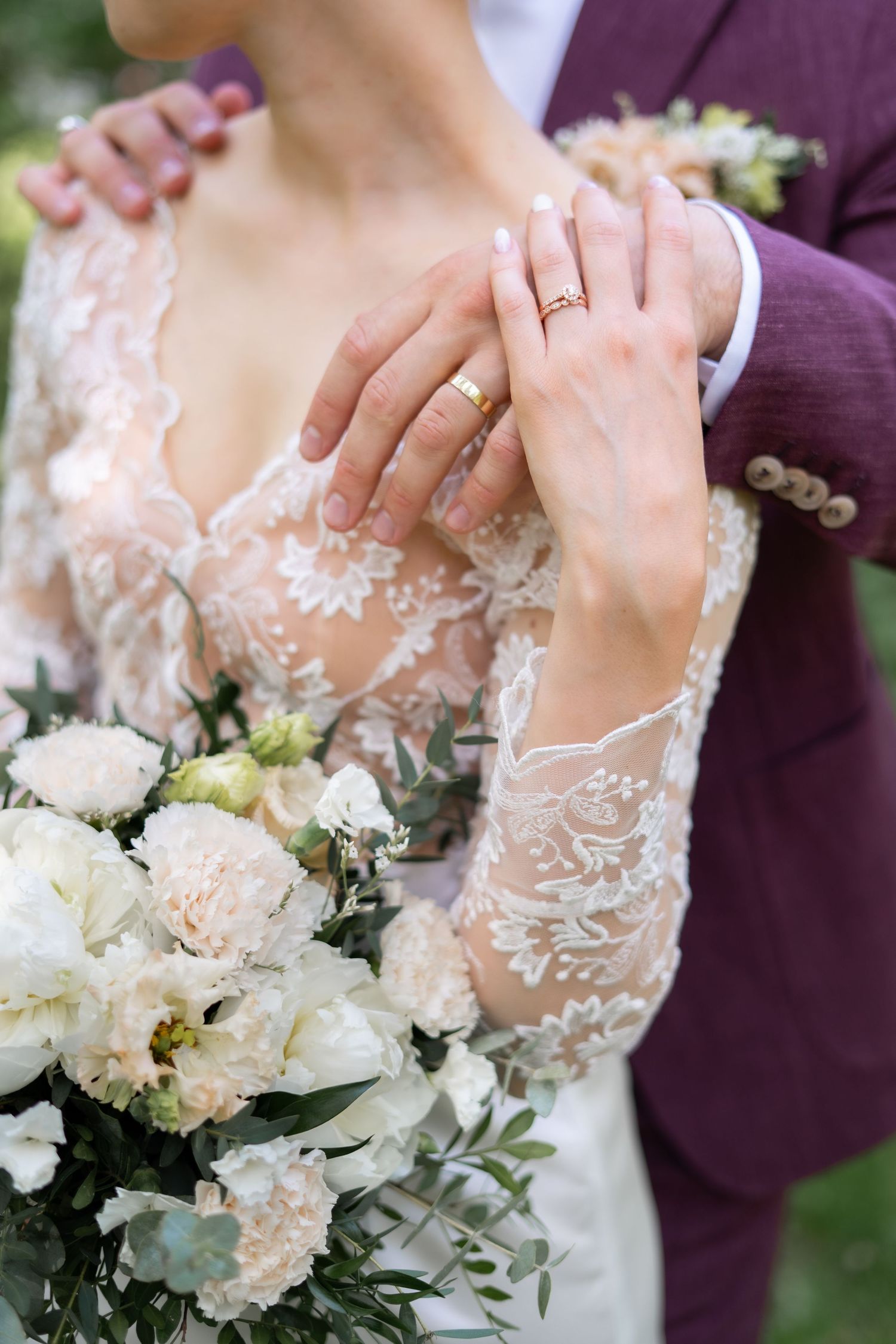 Close-up of newlyweds hands with gold wedding rings and elegant white floral bridal bouquet.