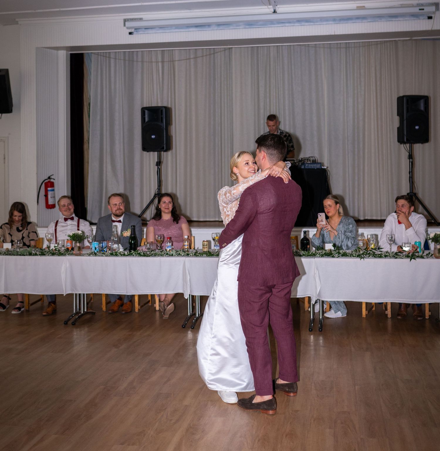 Bride and groom share their first dance at wedding reception while guests watch from decorated head table.