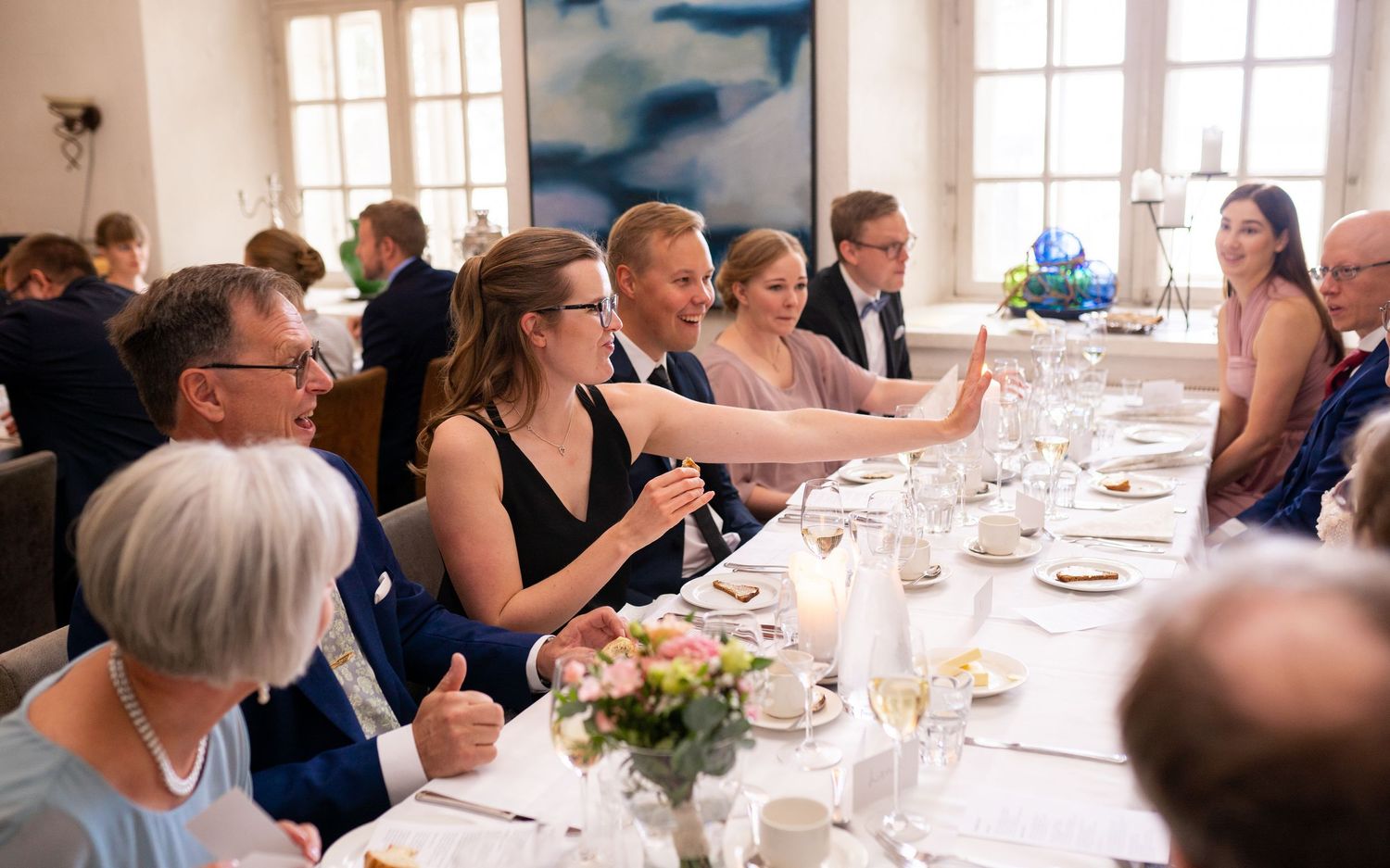 Wedding guests raising glasses in a toast during a formal reception dinner in a bright hall.