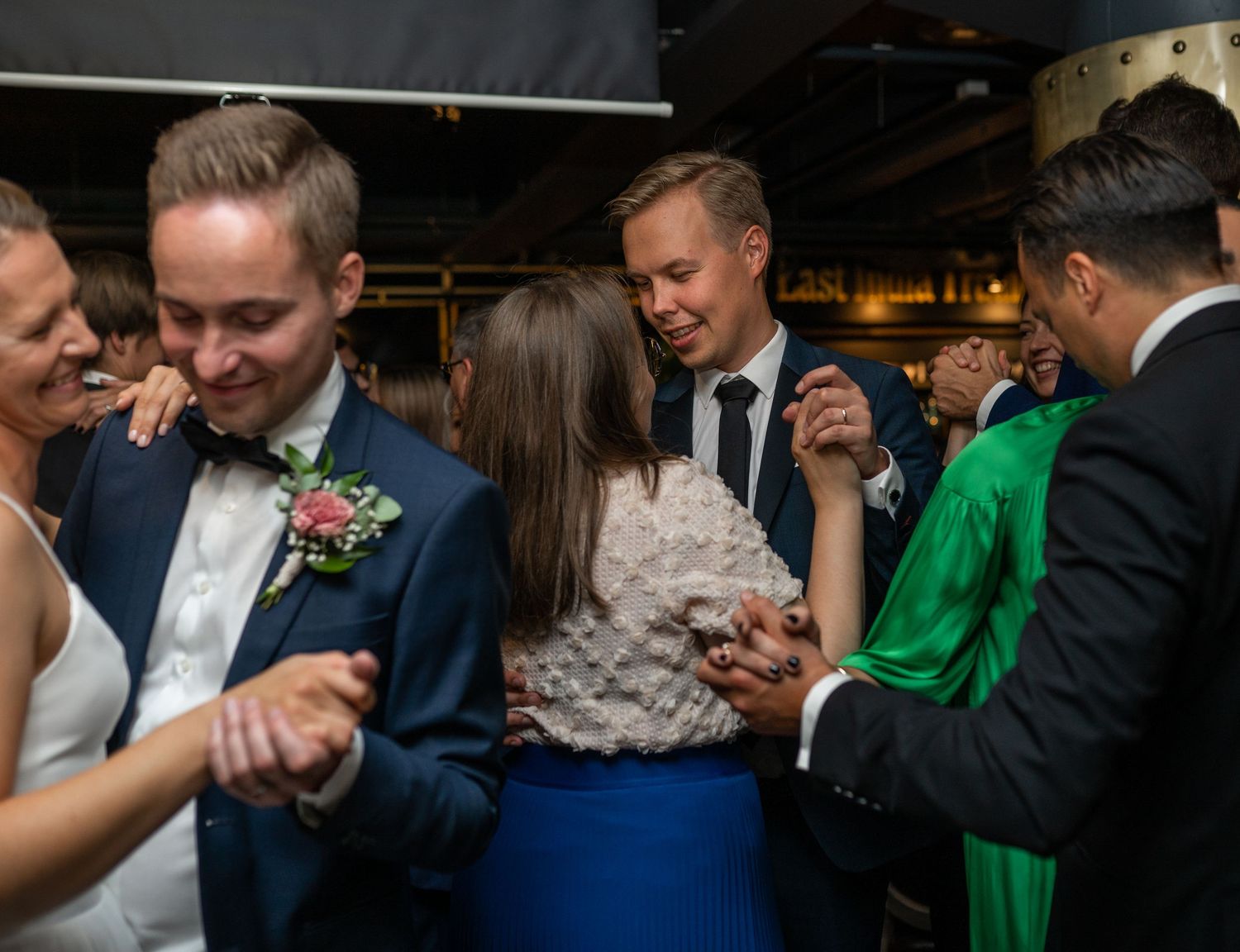 Wedding guests dancing joyfully together on the dance floor, with bride visible among the celebrating crowd.