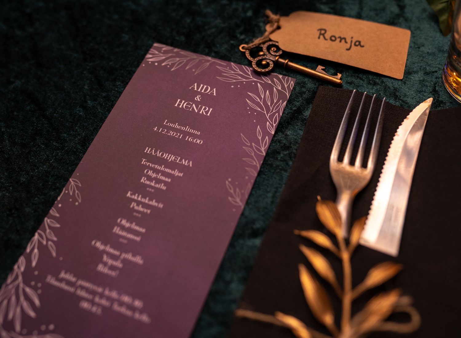 Elegant wedding menu card in deep purple with gold floral details, beside a fork, knife, and name tag reading Ronja.