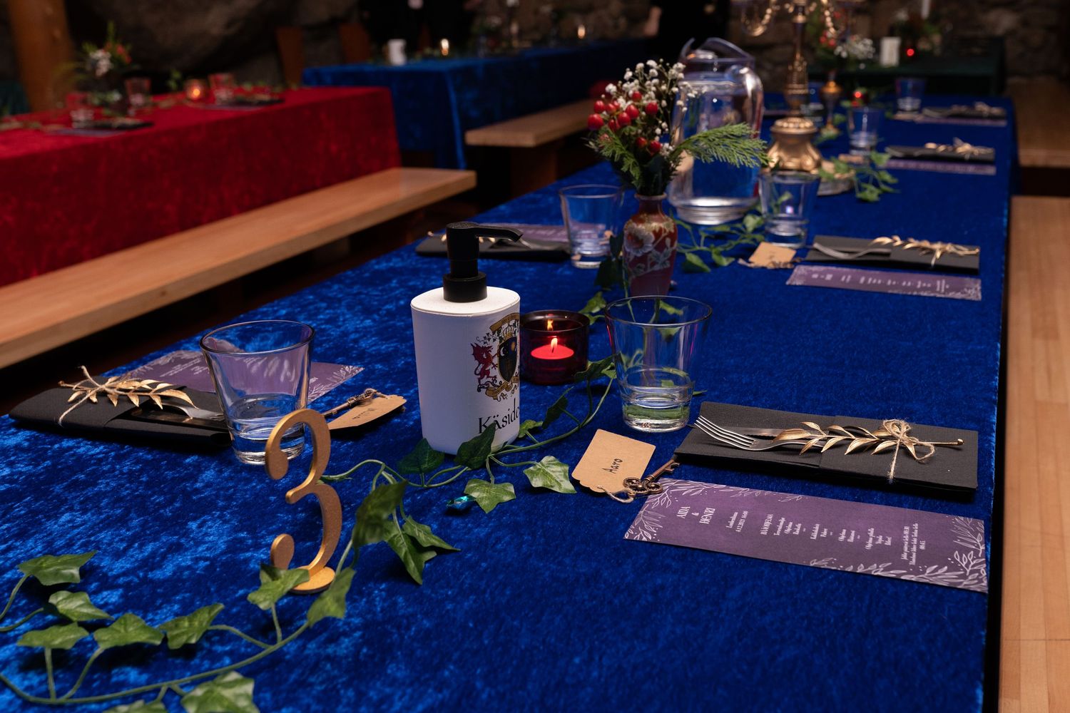 Elegant wedding table setting with blue velvet runner, greenery, candles, and gold number 3 table marker.