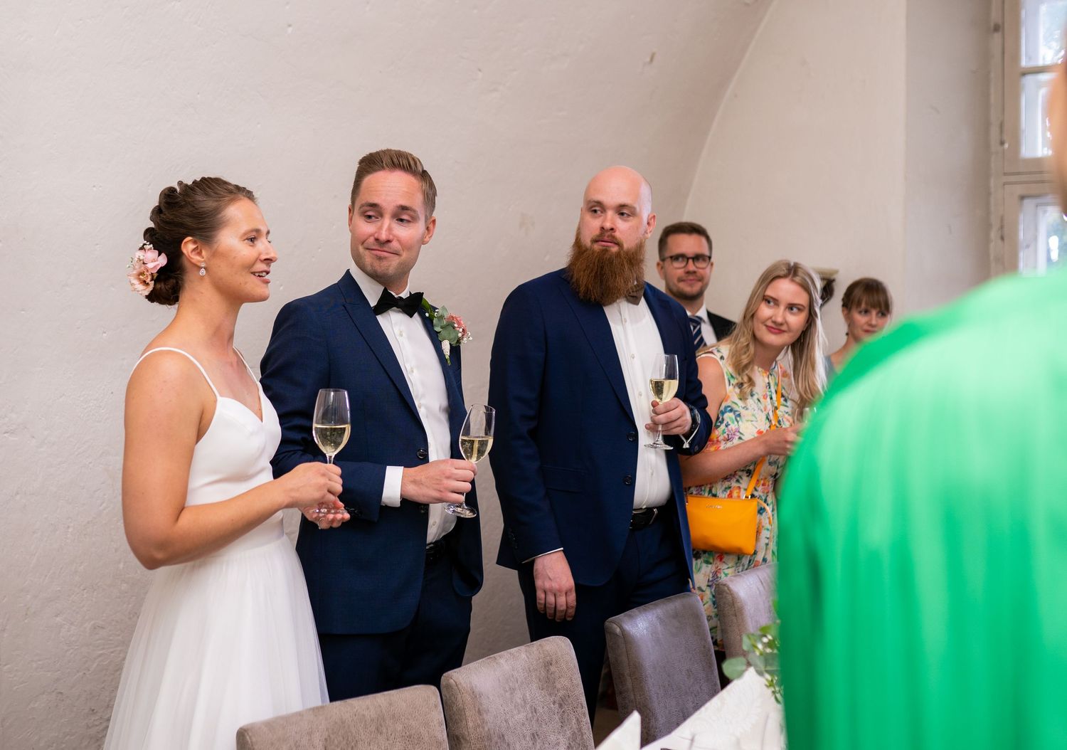 Wedding couple holding champagne glasses with bearded guest at elegant reception venue.
