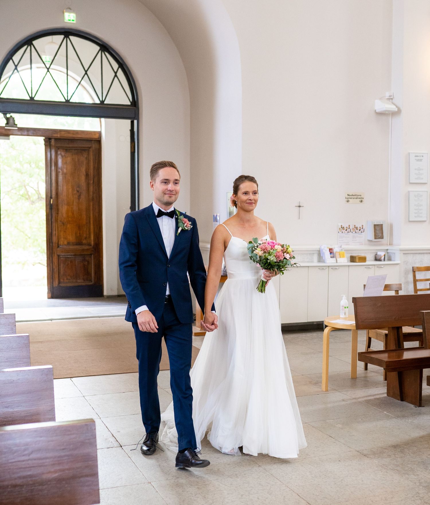Bride in white gown and groom in navy suit walking hand in hand down church aisle.