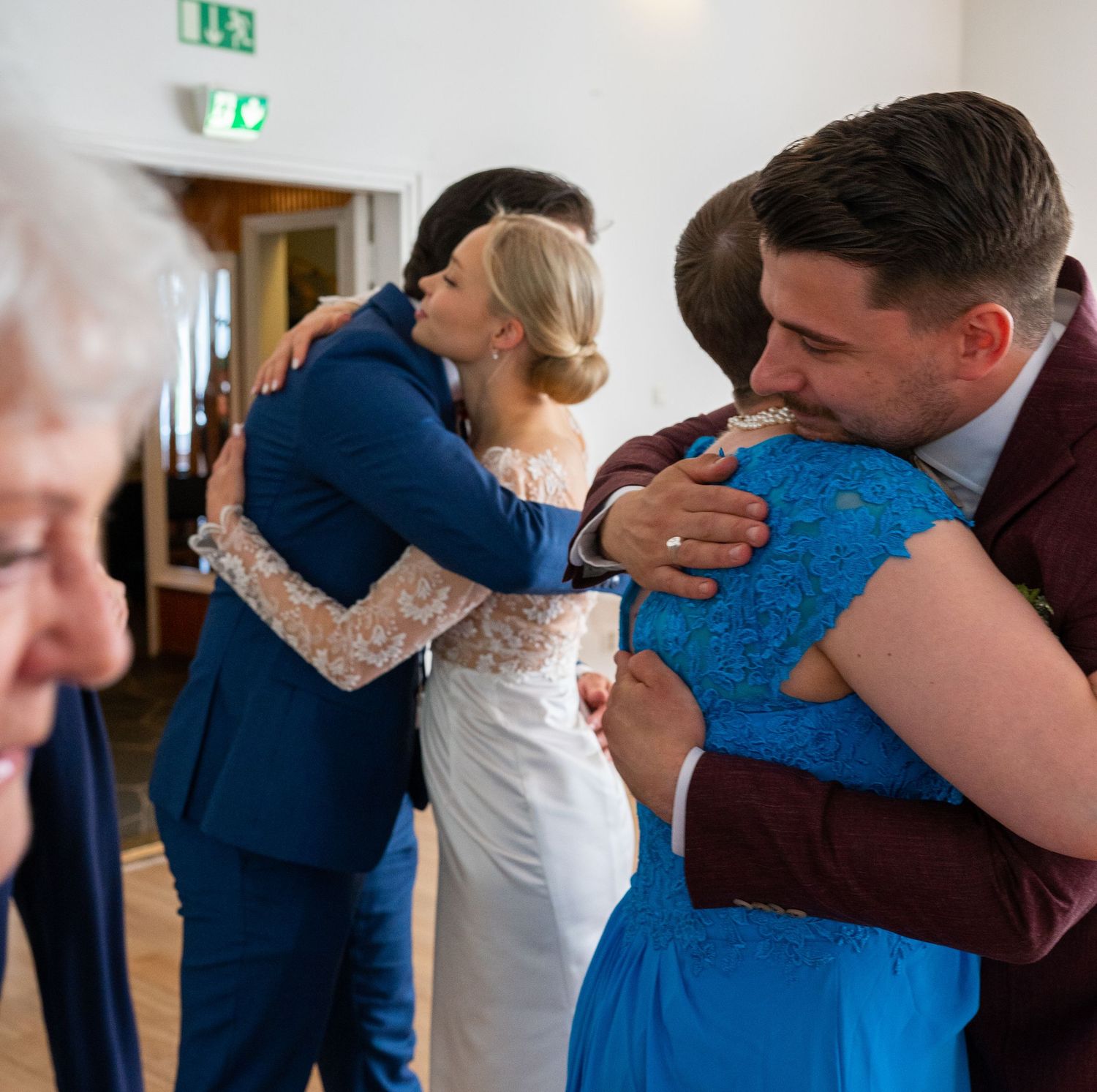 Bride and groom share heartfelt hugs with guests in blue outfits at wedding reception.