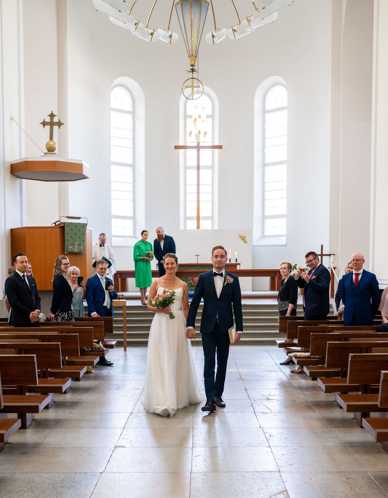 Newlyweds walking down church aisle after wedding ceremony with guests applauding.